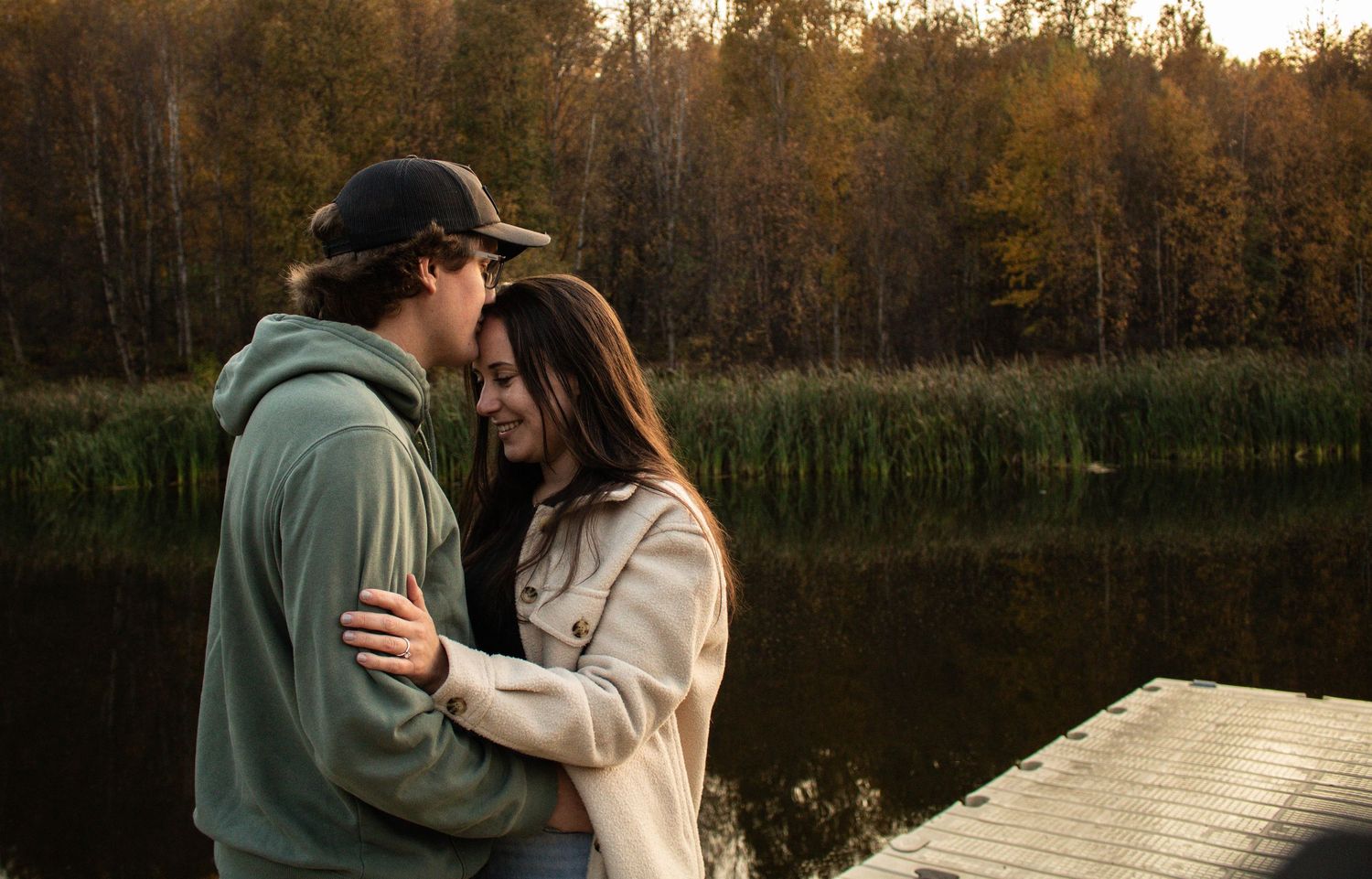 Romantic couple holding each other close by a peaceful lake during autumn sunset.