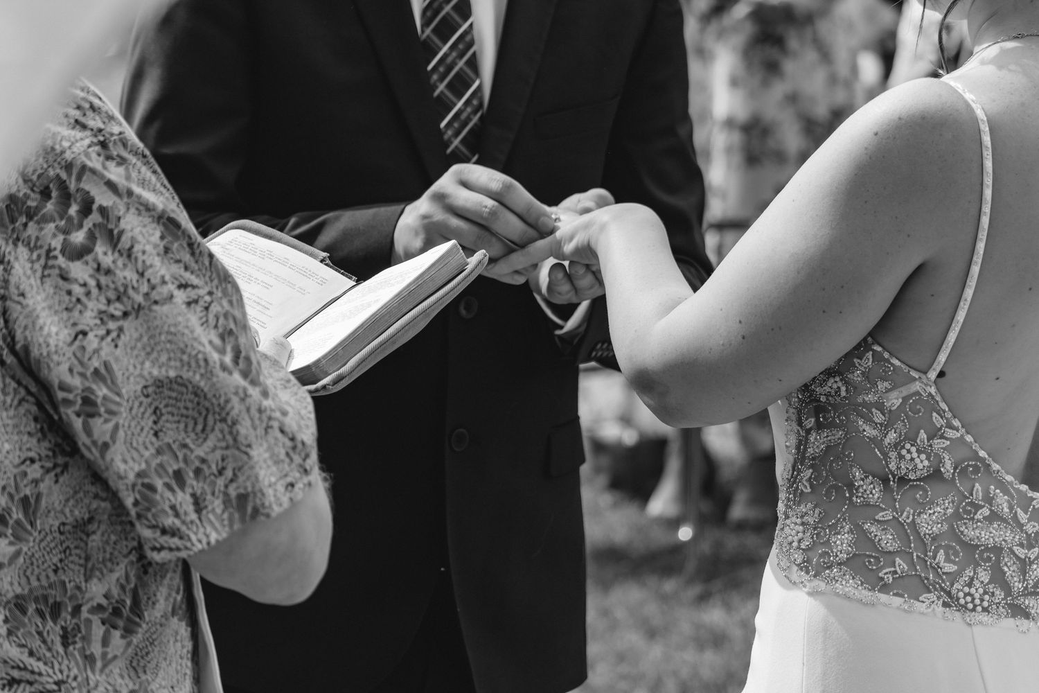 Black and white close-up of groom placing wedding ring on brides finger during ceremony.