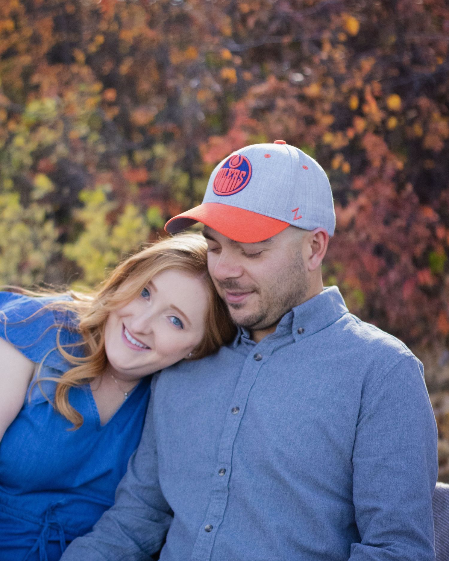 Smiling couple embracing outdoors in autumn with colorful fall foliage in the background.