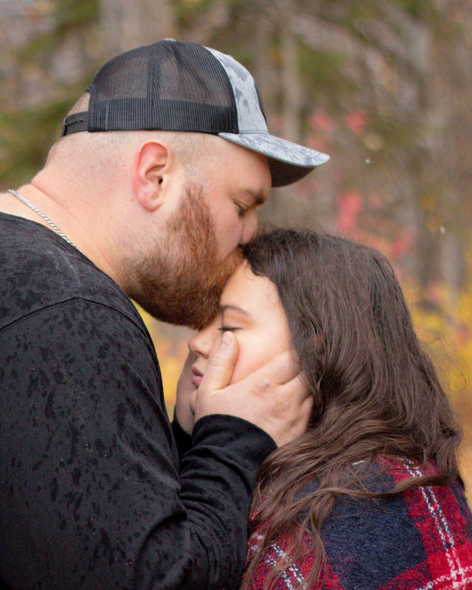 Couple sharing a sweet forehead kiss outdoors in autumn, woman smiling with eyes closed in fall setting.
