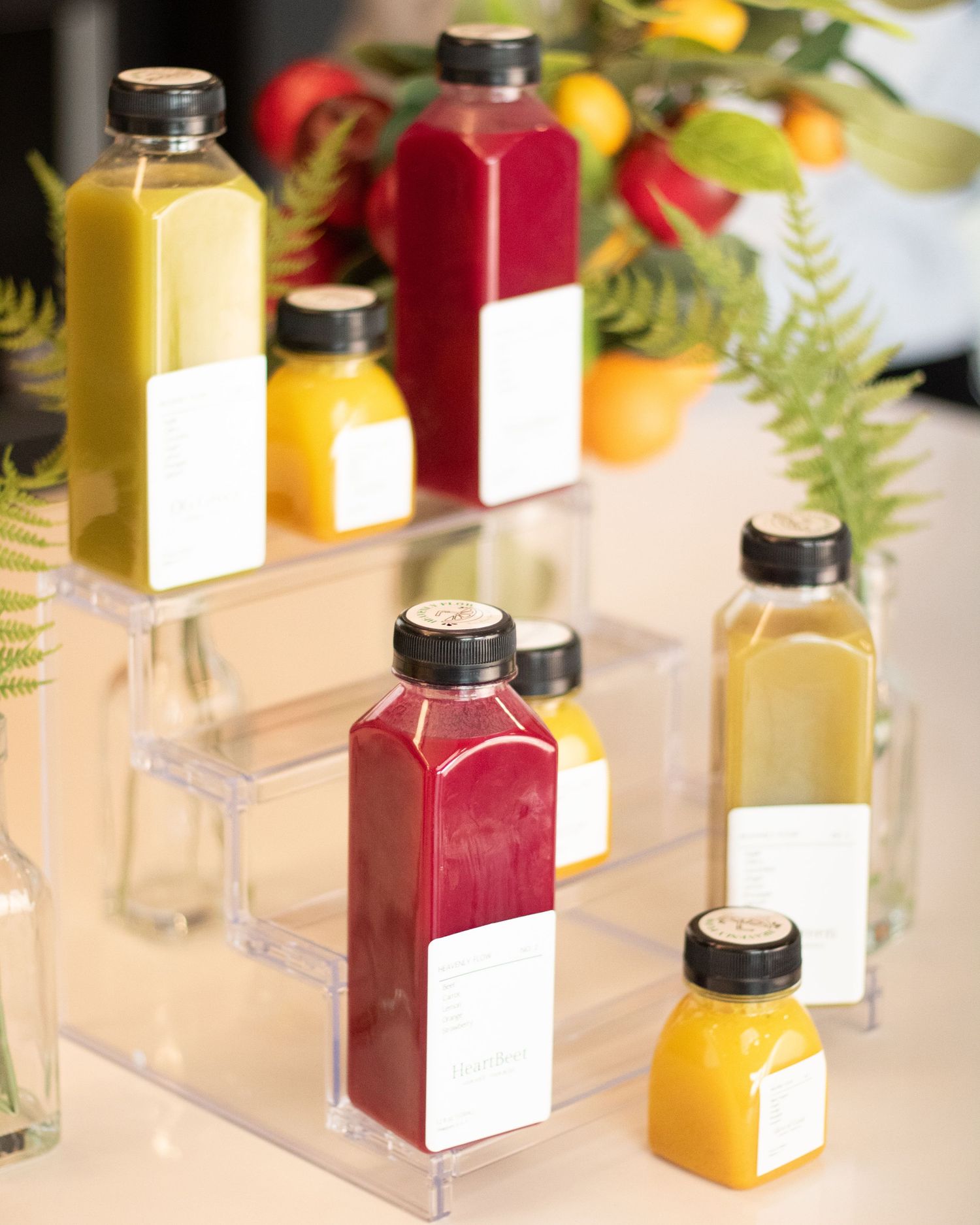Colorful juice bottles displayed on clear acrylic risers with floral arrangement behind.