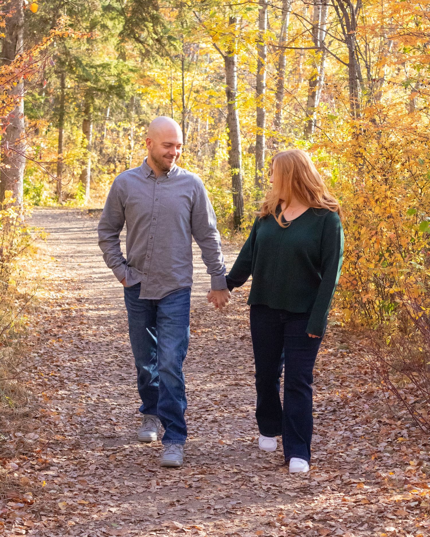 Happy couple holding hands walking on a leaf-covered forest path in autumn foliage.