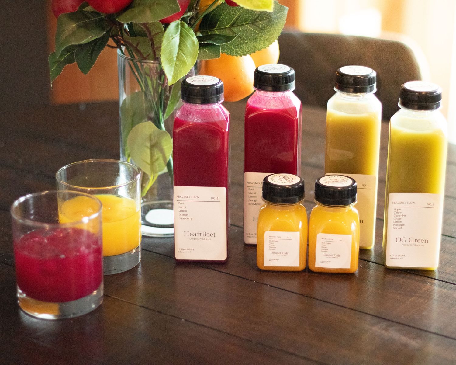Assorted fresh cold-pressed juices in bottles and glasses displayed on rustic wooden table.