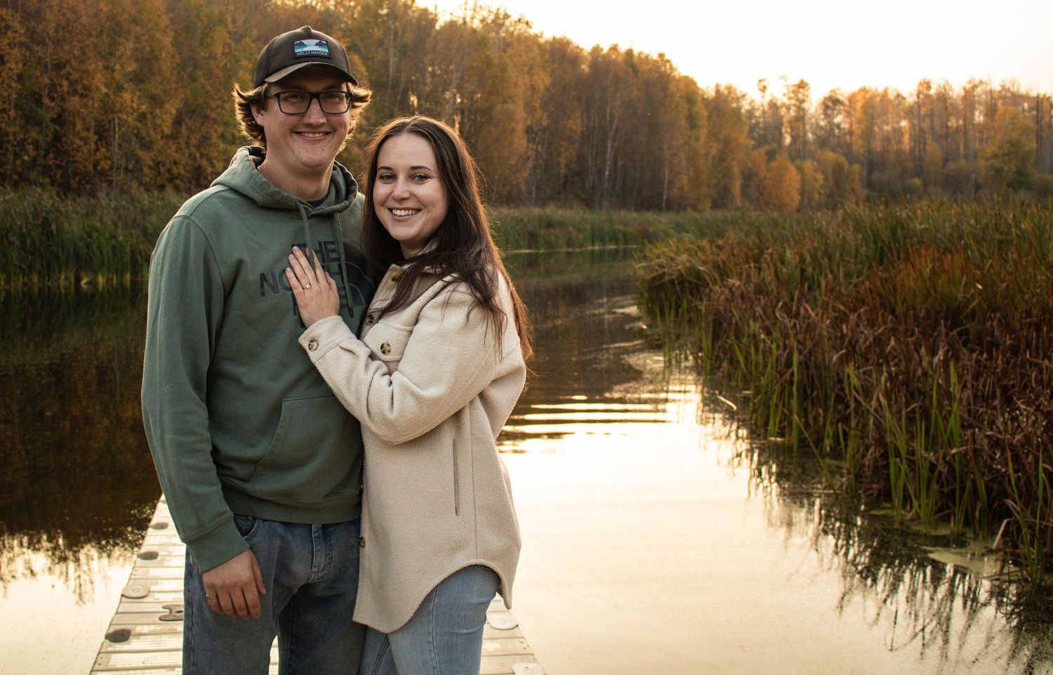 Happy couple posing together on a wooden dock surrounded by vibrant fall foliage.