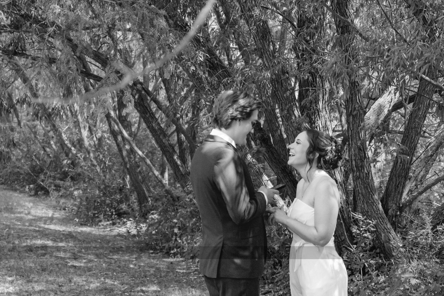 Black and white photo of bride and groom sharing an intimate moment among trees on wedding day.