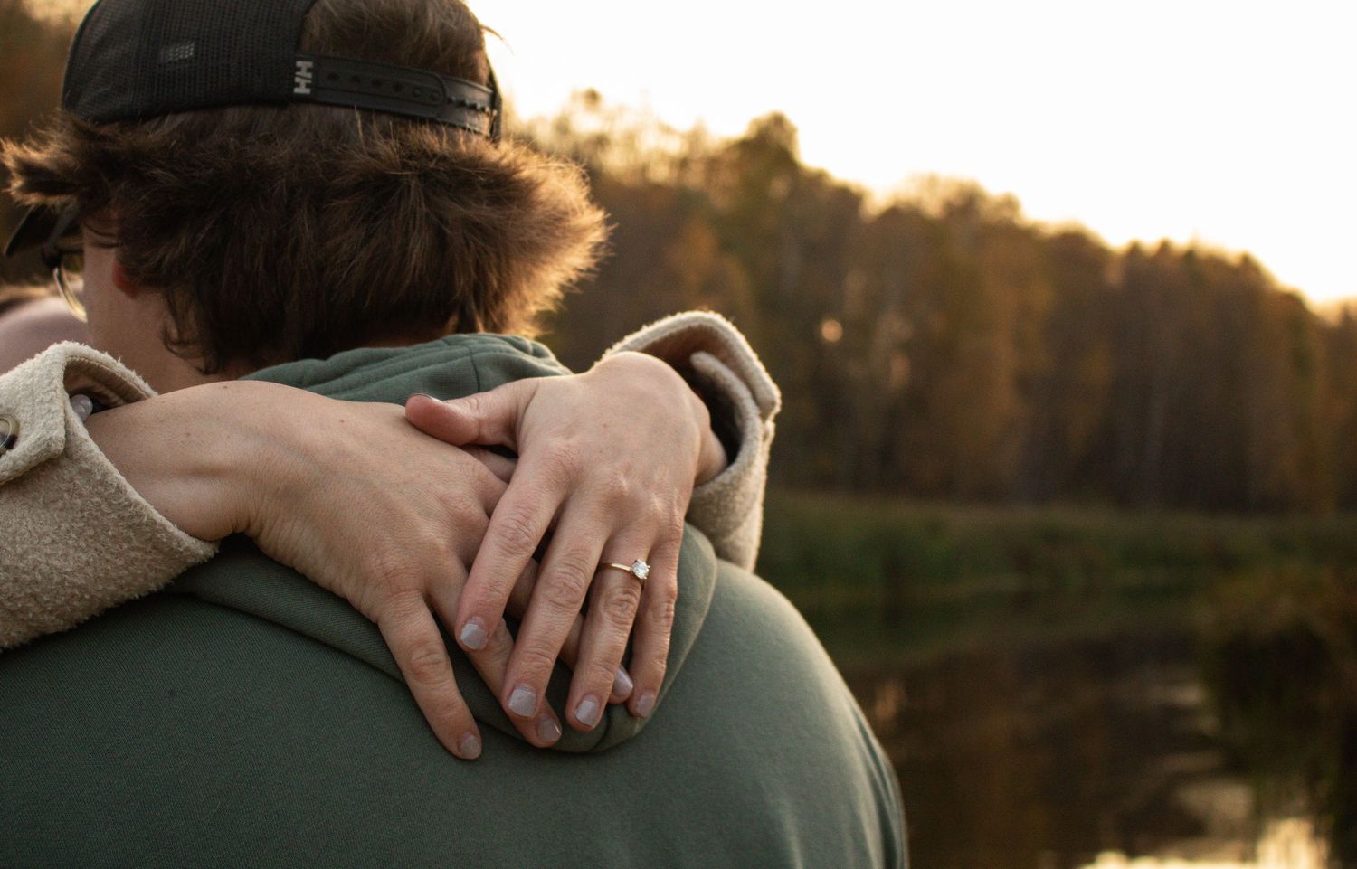 Detail shot of couple hugging near a lake, woman's engagement ring visible on hand.