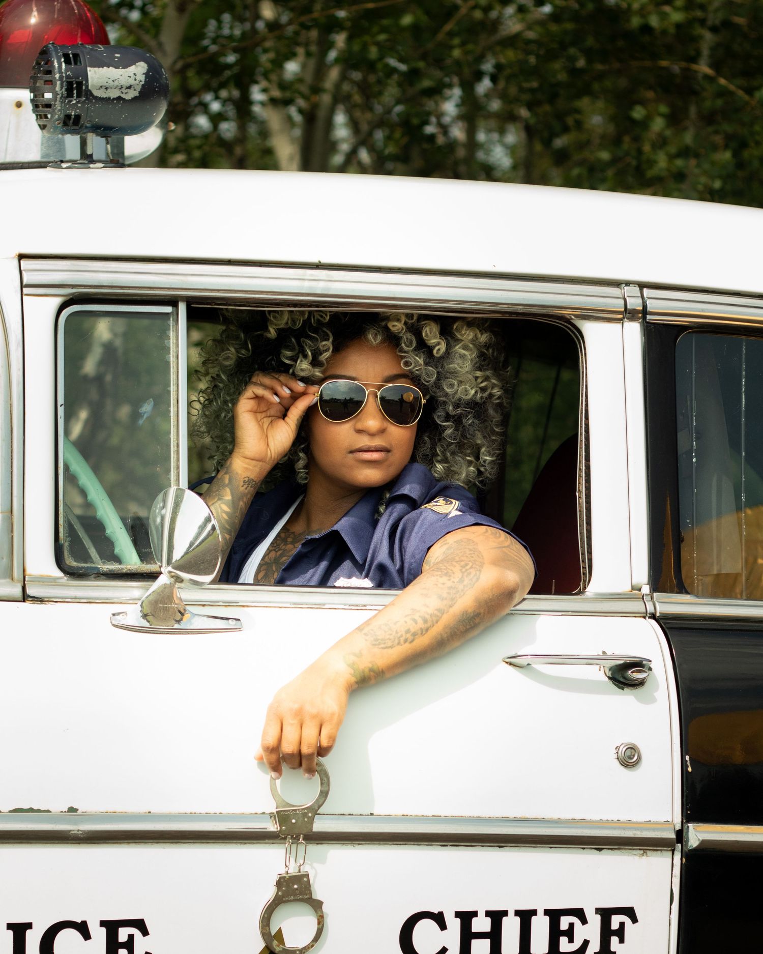 A person in a police uniform wearing aviator sunglasses leans from a vintage Police Chief vehicle window.