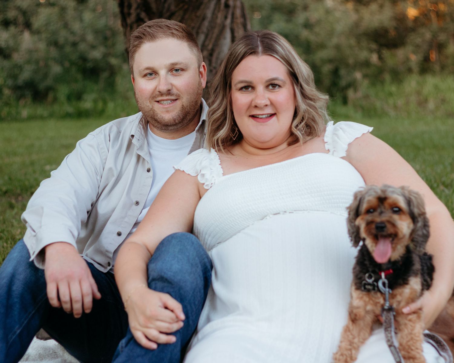 Happy couple sitting outdoors with their adorable brown dog during a casual portrait session.
