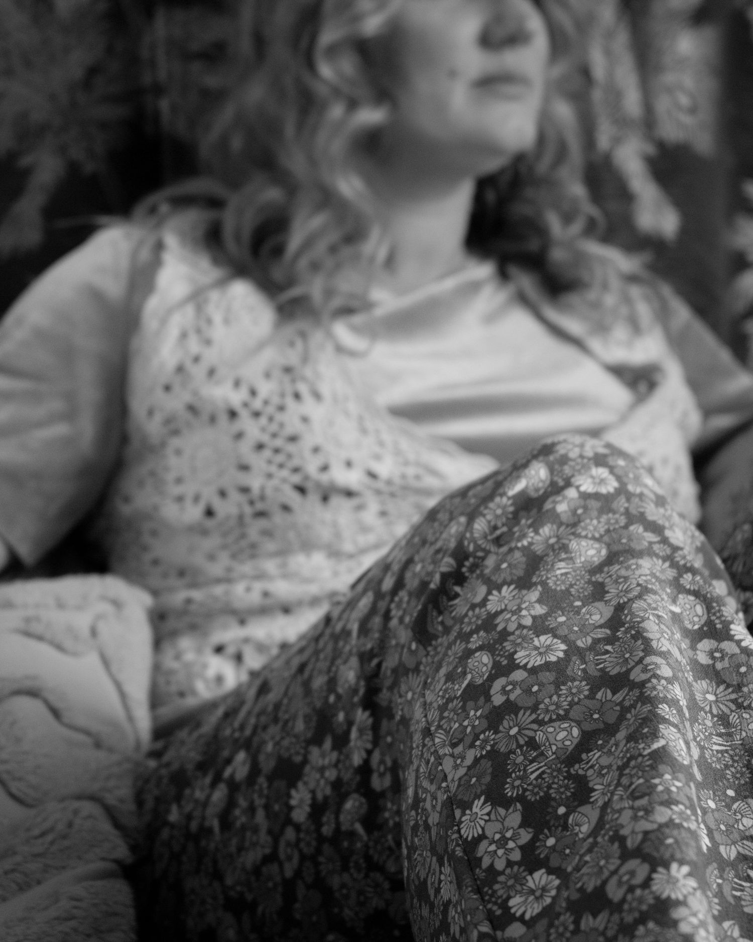 Close-up black and white photo of woman in lace top reclining on a couch with floral pants.