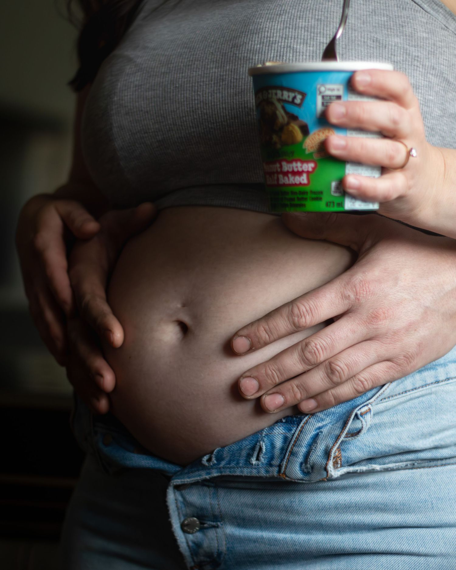 Pregnant woman holding Ben & Jerry's Peanut Butter ice cream pint while partner touches baby bump.