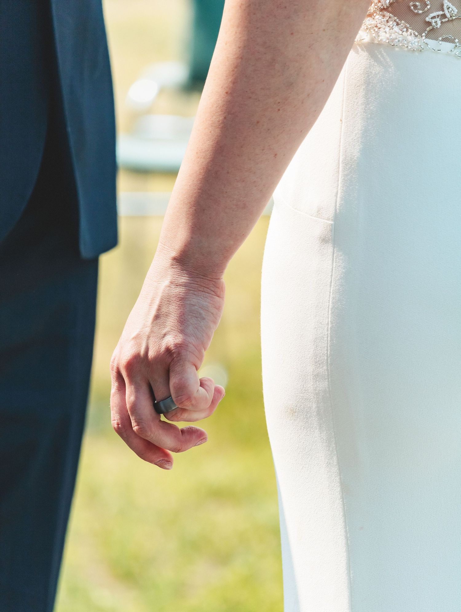 Close-up of bride and groom holding hands showing grooms wedding ring after the ceremony.