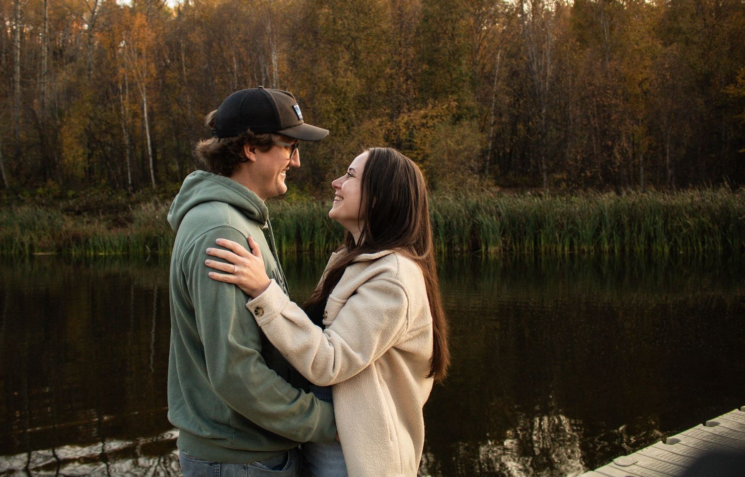 Happy young couple smiling and embracing each other on a lakeside dock in autumn scenery.