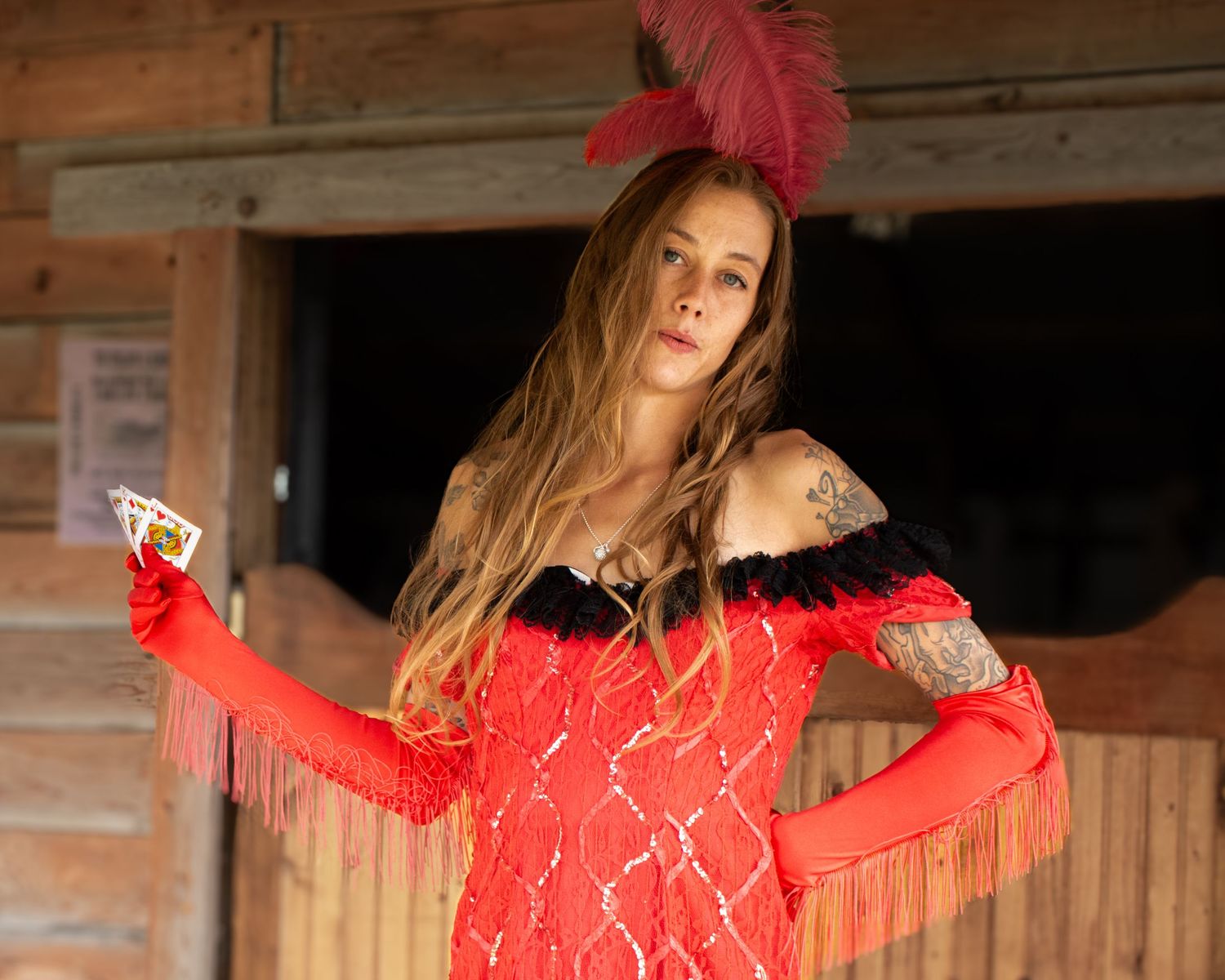 Woman in a red sequined saloon costume with feather headpiece holding a playing card.