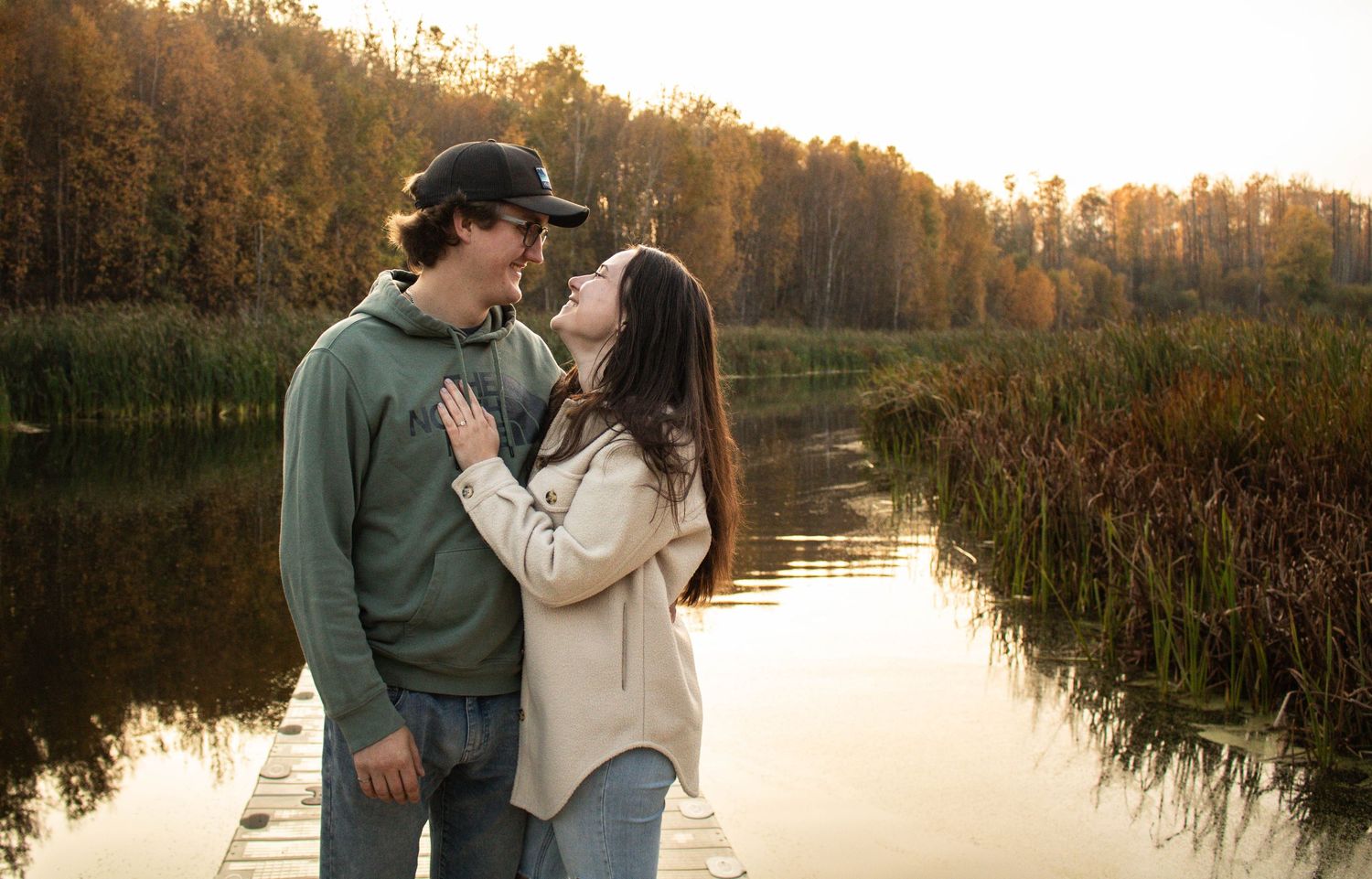Couple gazing into each other's eyes on a dock with golden autumn lake backdrop.