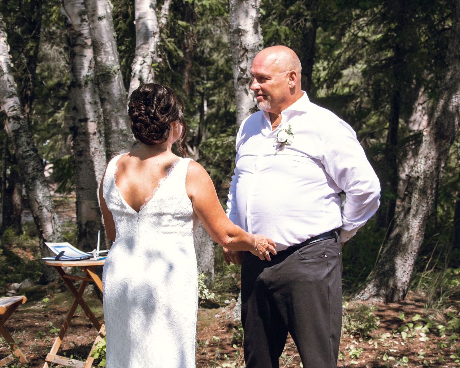 Bride and groom holding hands during outdoor forest wedding ceremony among birch trees.