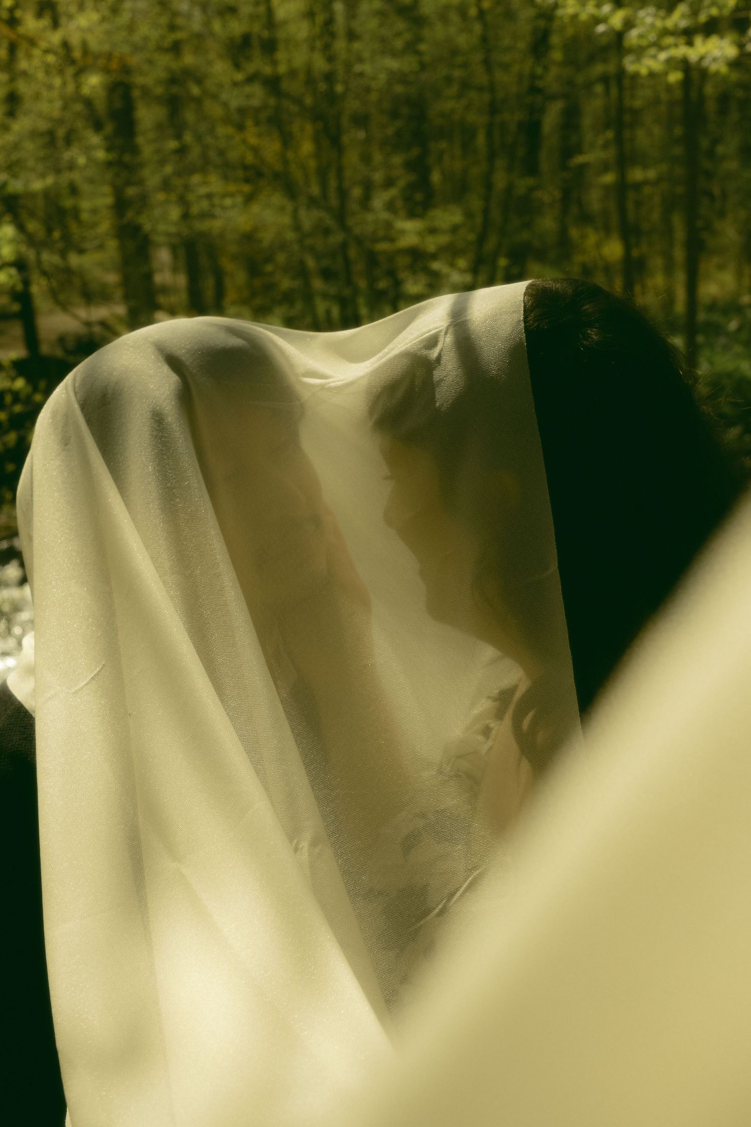 Artistic portrait featuring draped white fabric against a dark forest background.