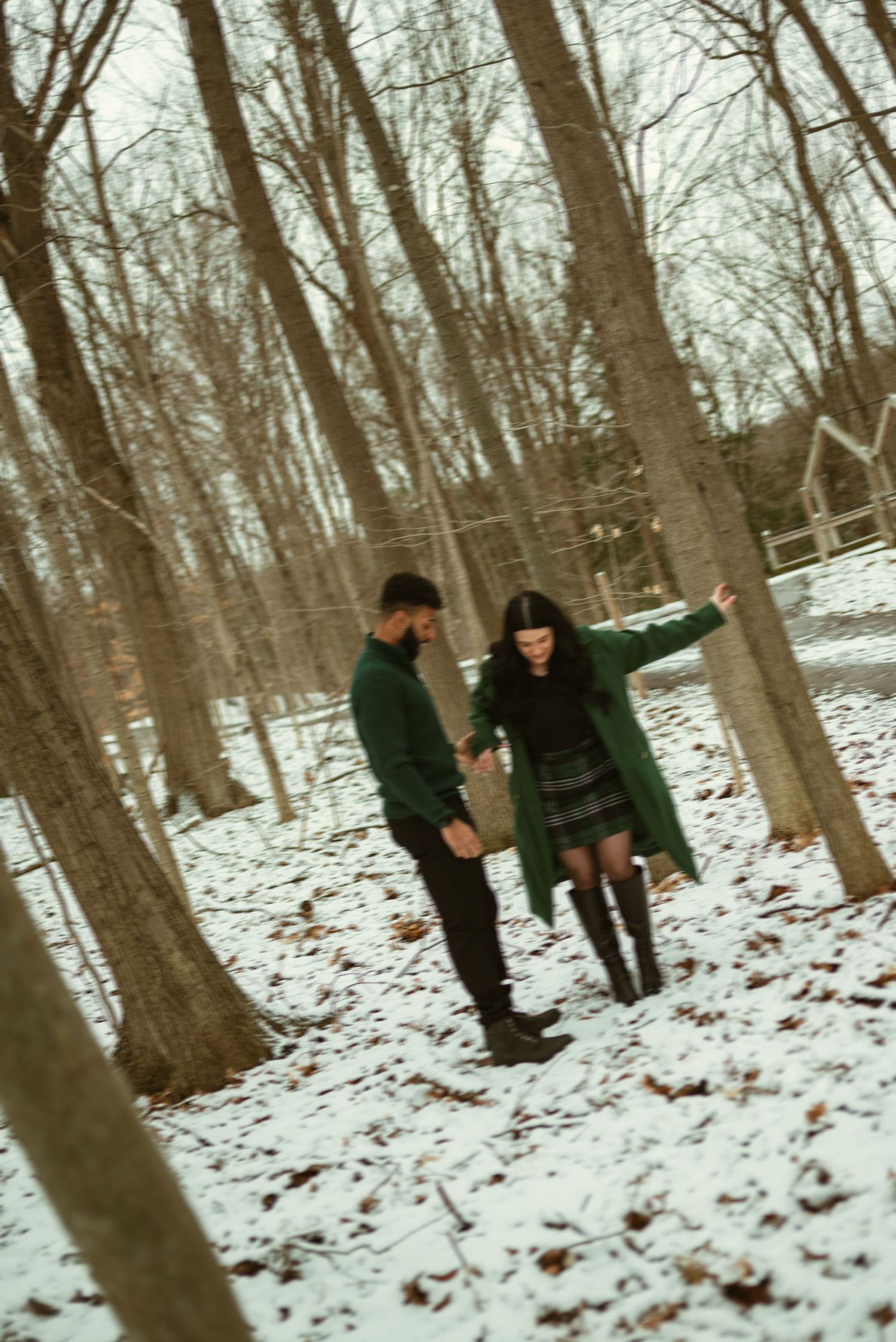 A couple in dark winter coats walks together through a snowy wooded area on a winter day.