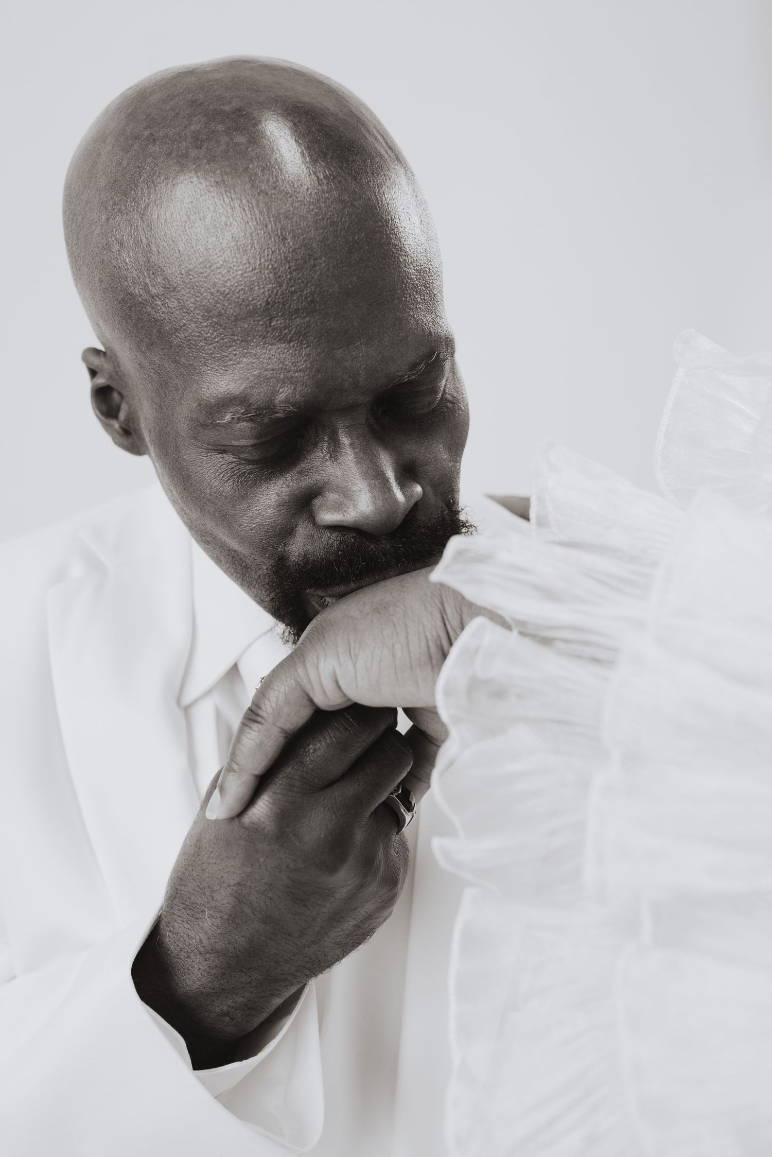 Black and white portrait of a bald man in white shirt kissing a hand with a ring.