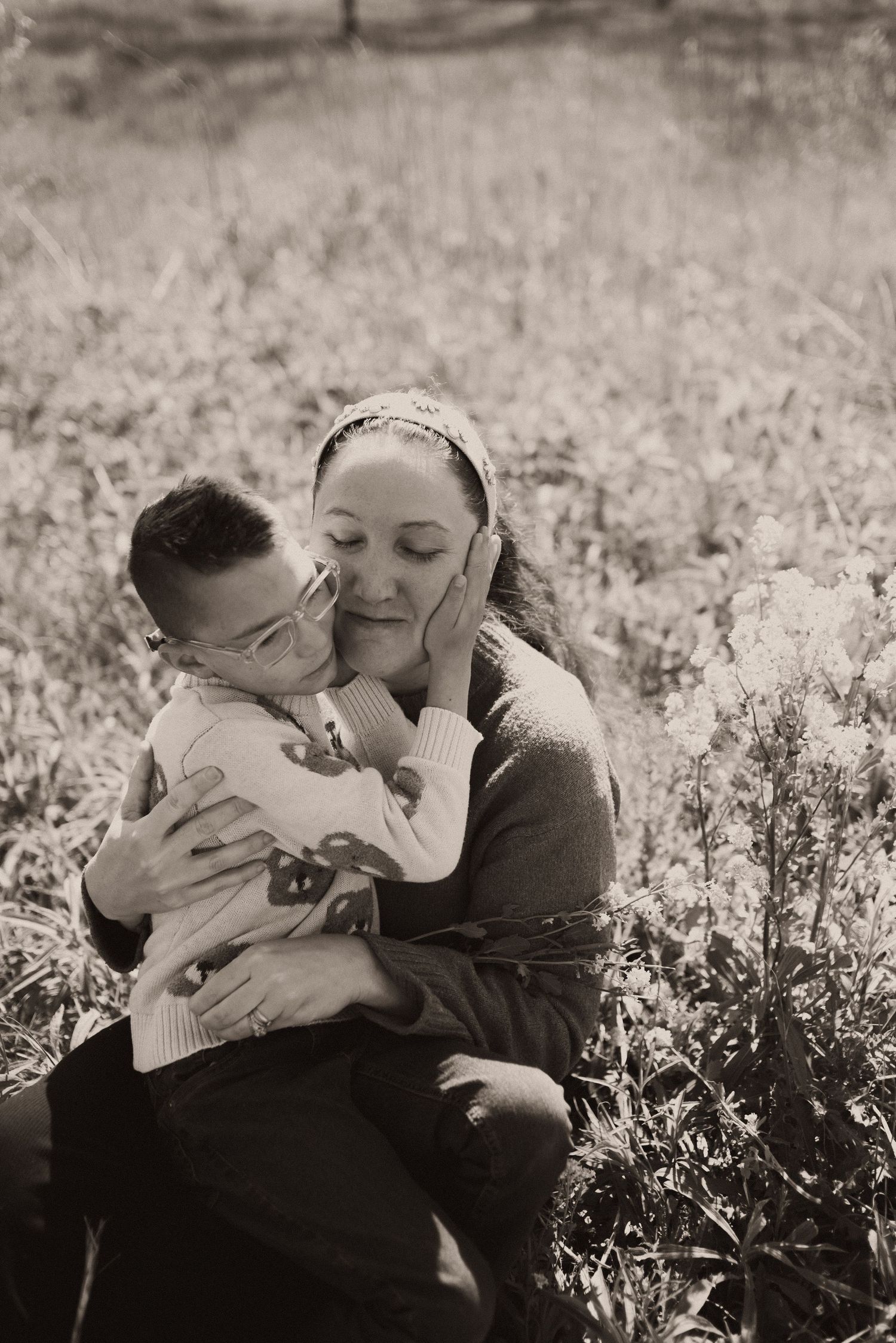 A mother and young son share a tender embrace in a field, captured in sepia tone.