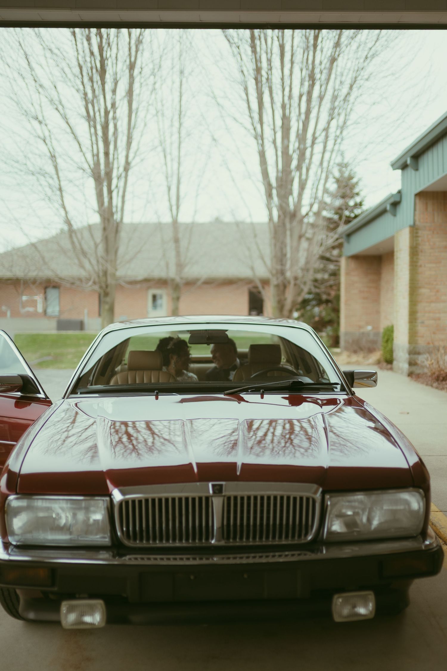 A classic burgundy Jaguar sedan parked in a garage with a couple visible through the windshield.