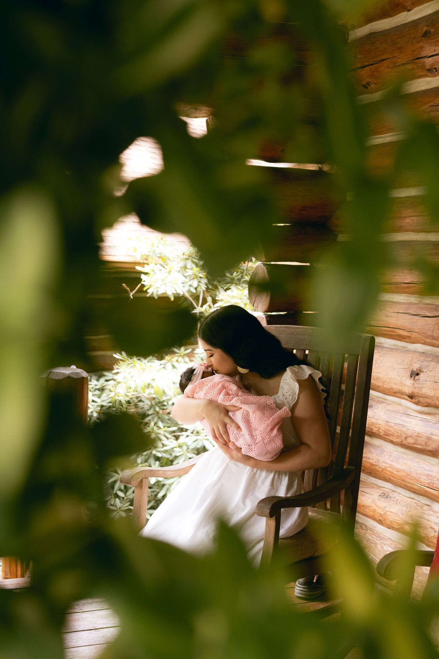 A tender moment captured through leaves as sparklers create magical light trails against a rustic wooden wall.