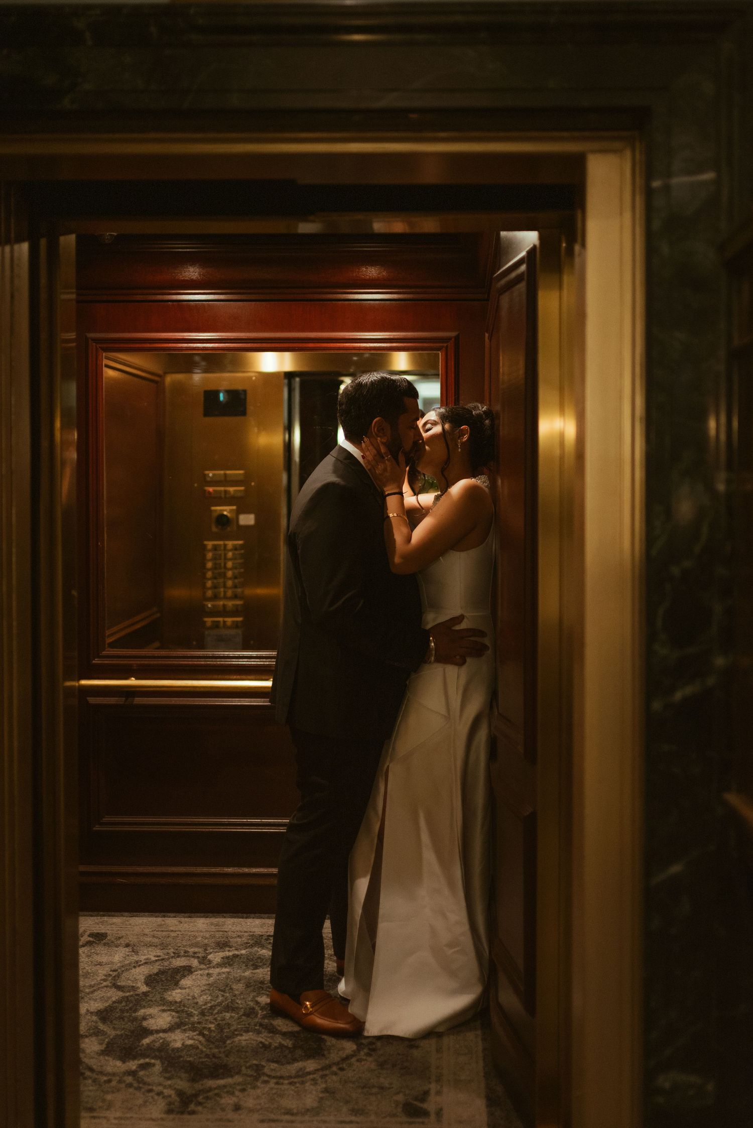 Bride and groom sharing a romantic kiss inside an elegant gold elevator on their wedding day.