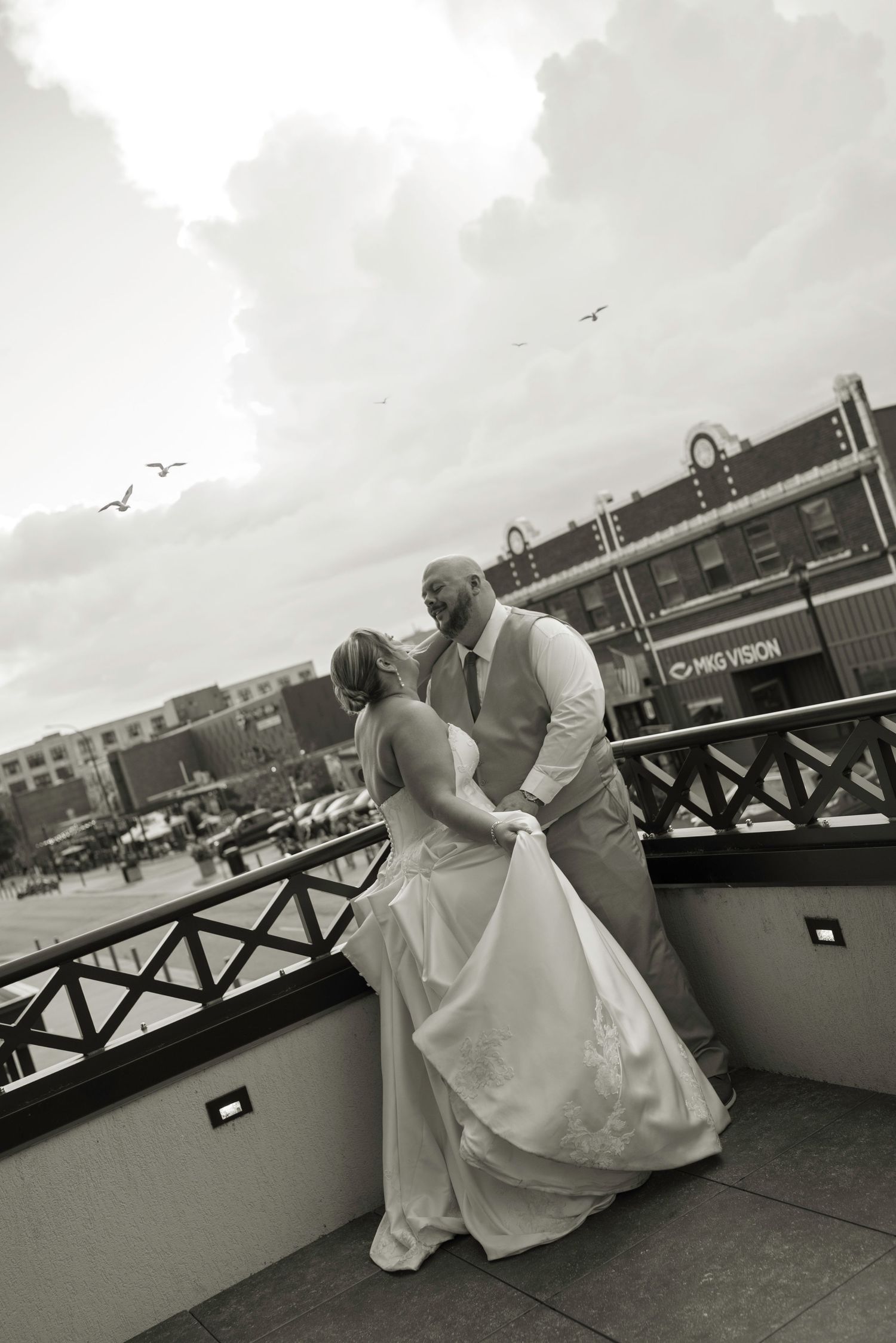 Black and white photo of a bride and groom sharing a romantic moment on a waterfront balcony on their wedding day.