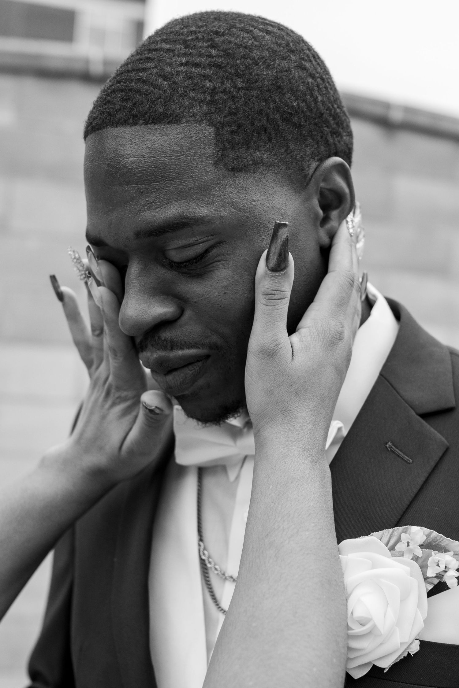 Black and white wedding photo of groom in suit with boutonniere, bride's hands tenderly cradling his face.