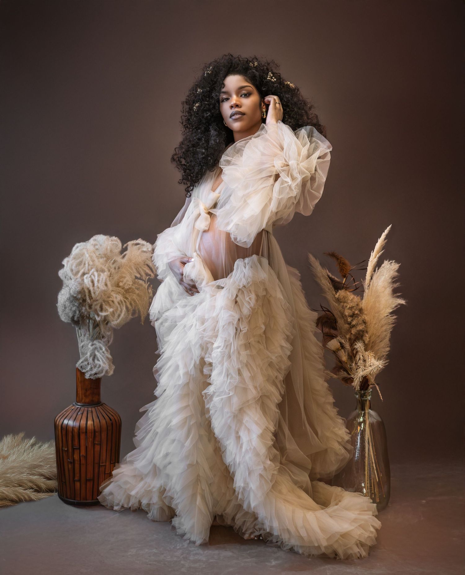 A glamorous fashion photoshoot featuring a flowing white tulle gown with dramatic ruffles against a dark studio backdrop.