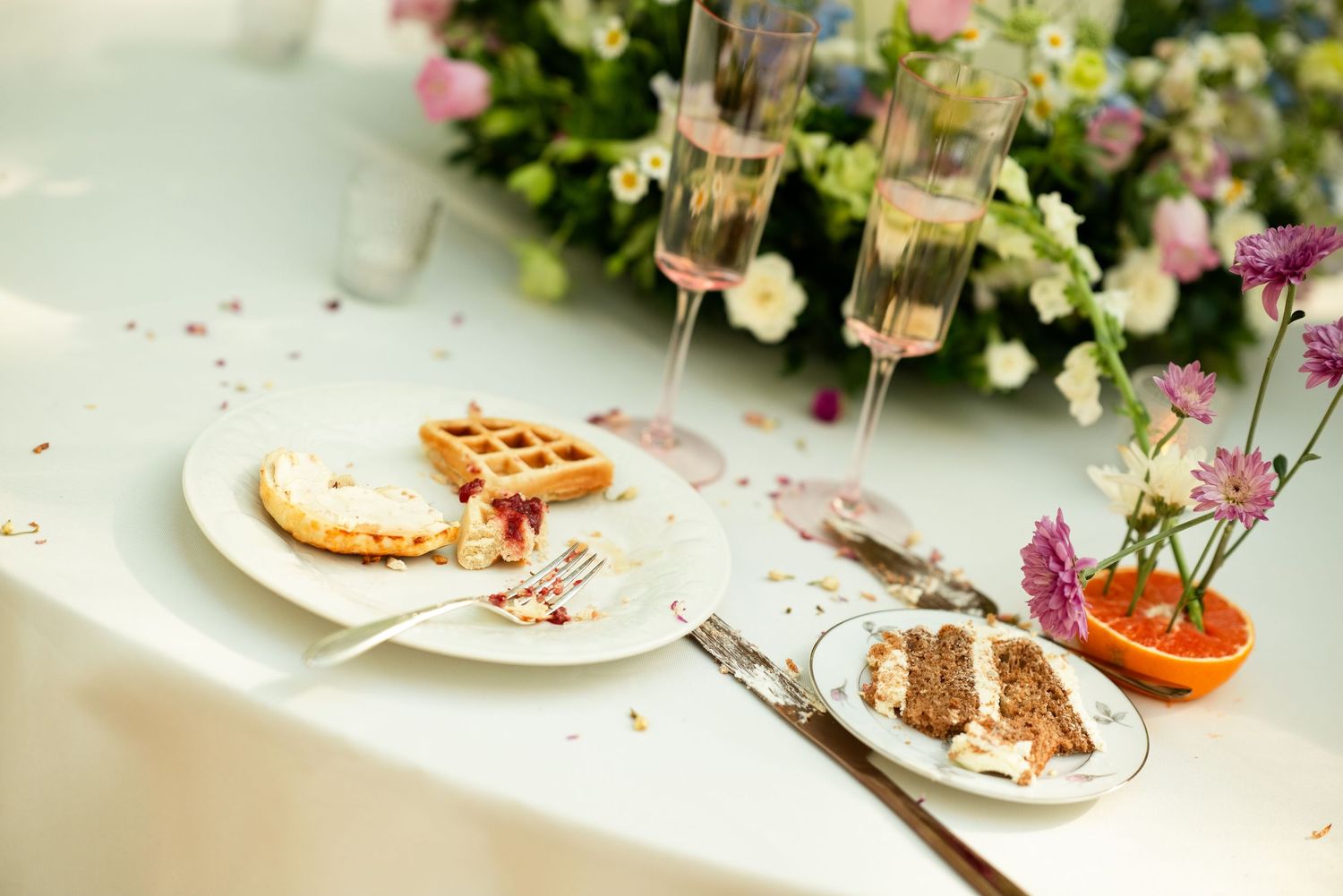 Elegant wedding table with a waffle, layered cake slice, champagne flutes, and fresh flowers in soft pastel tones.