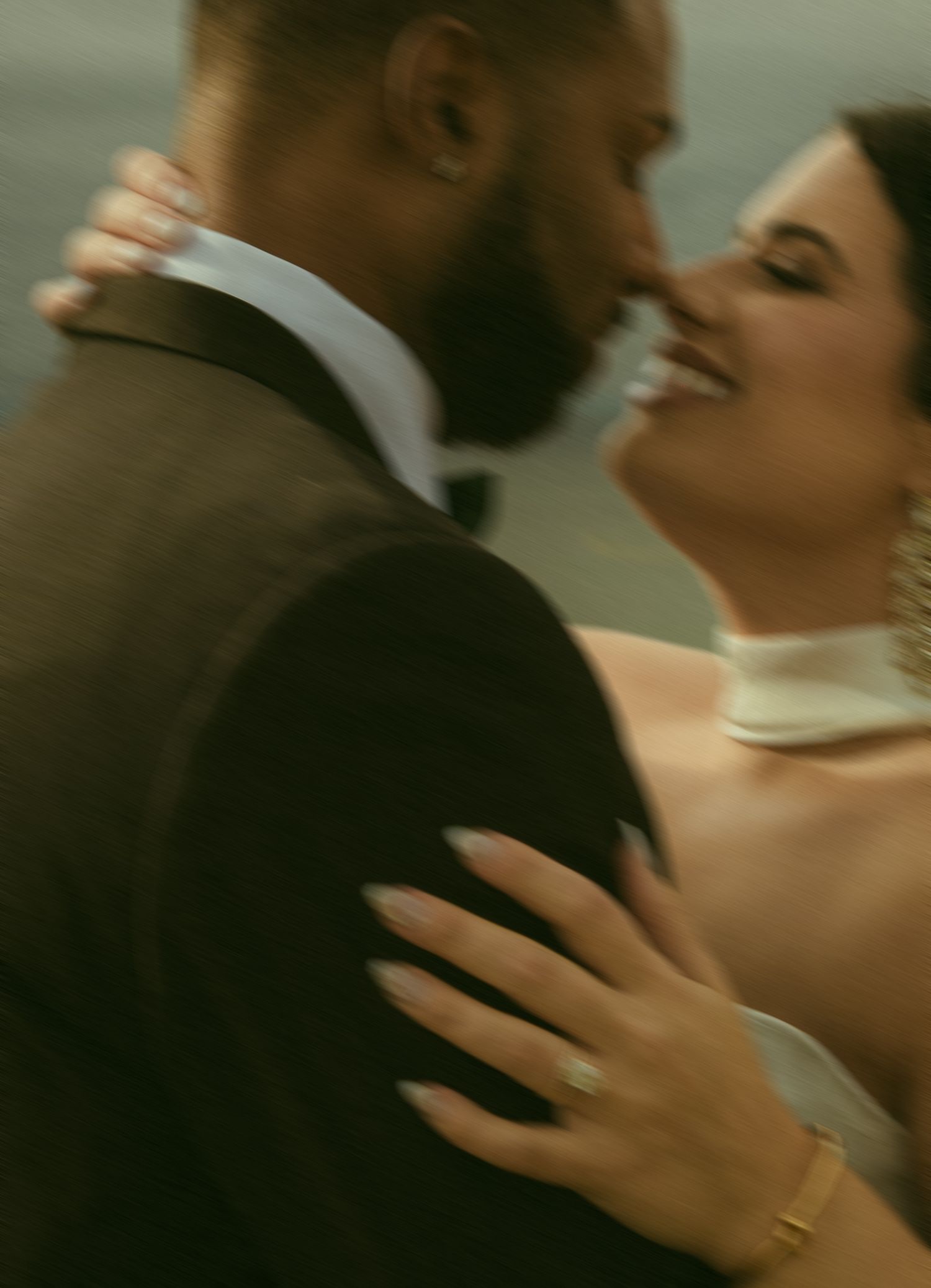 A joyful bride and groom share an intimate moment, with the bride smiling and wearing a gold bracelet and engagement ring.