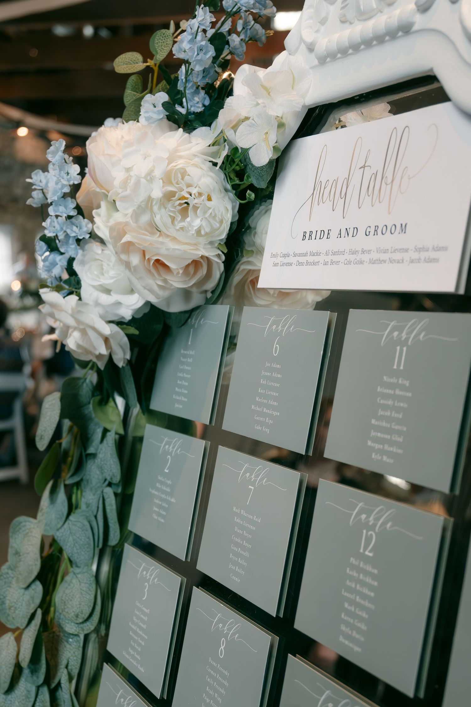 Wedding seating chart display with gray cards decorated with blue and white floral arrangements.