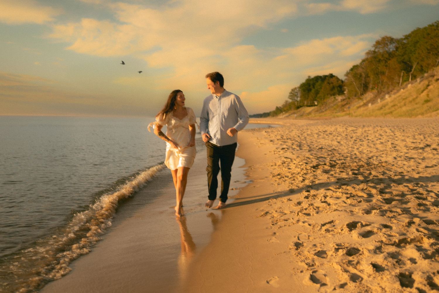 Two people walking along a sandy beach at sunset with golden light illuminating their path.