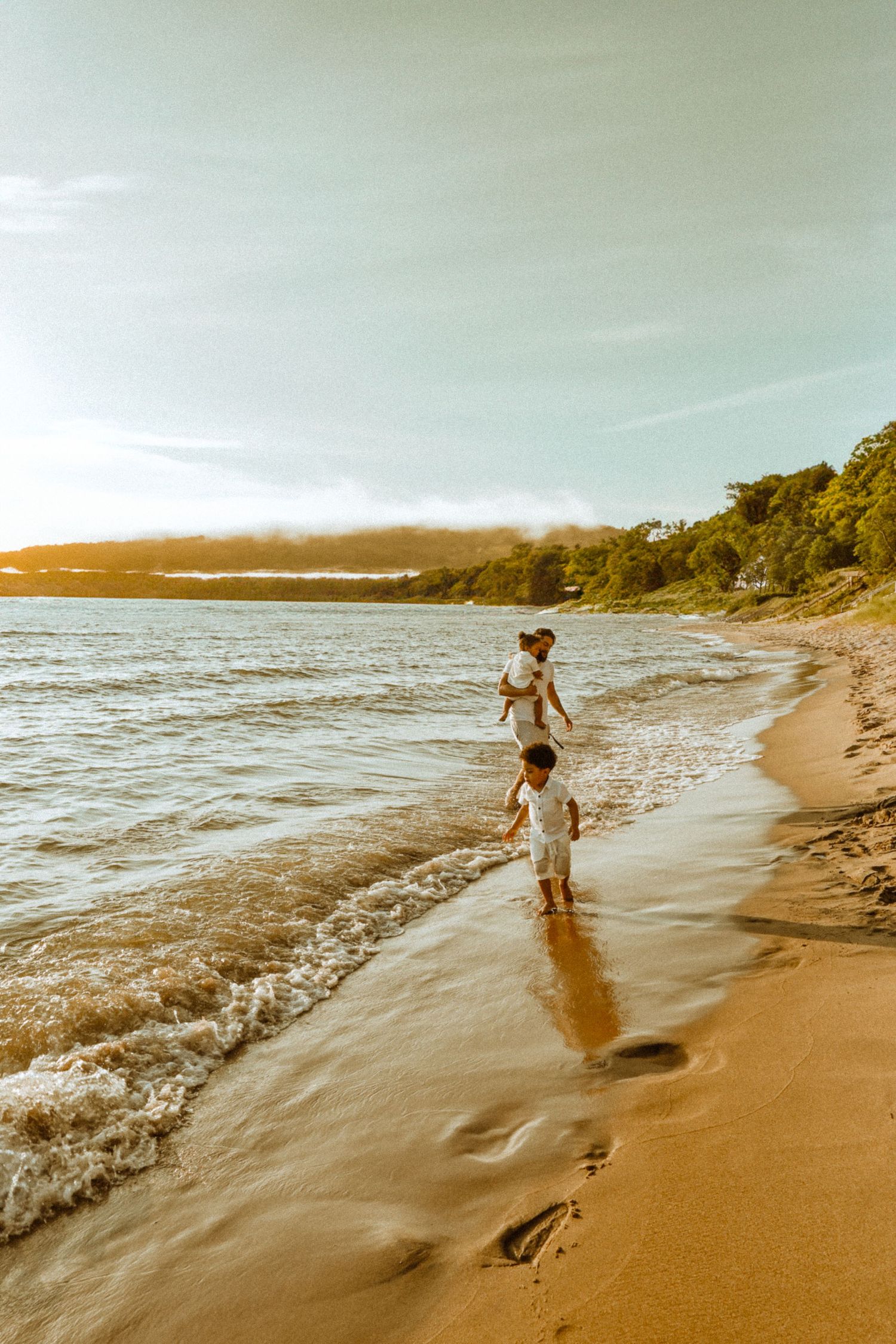 Two figures playing in ocean waves at sunset on a beautiful sandy beach.