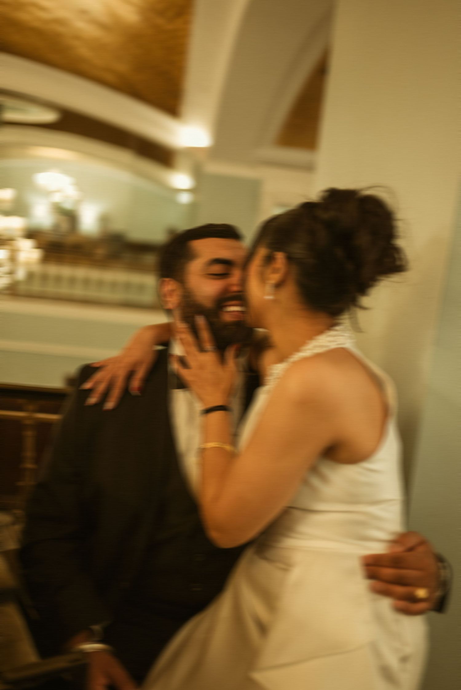 Couple sharing a joyful embrace at an indoor wedding reception, bride in white dress, groom in dark suit.
