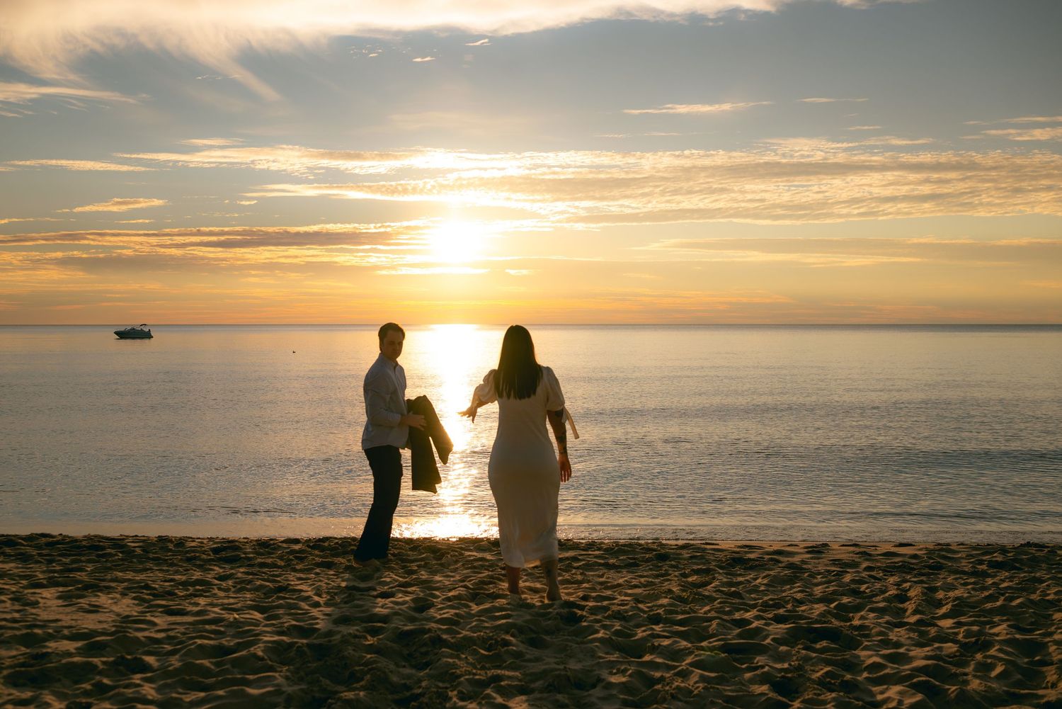 Silhouettes of people walking along a beach at sunset with dramatic orange and gold sky over the ocean.