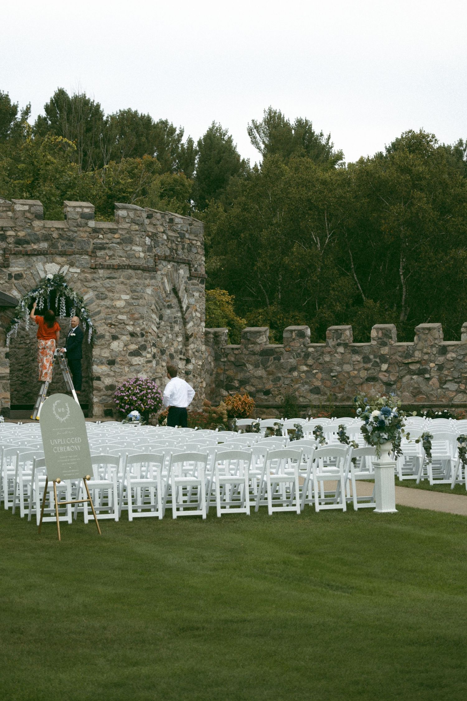 White chairs arranged in rows for an outdoor wedding ceremony against a rustic stone wall backdrop.