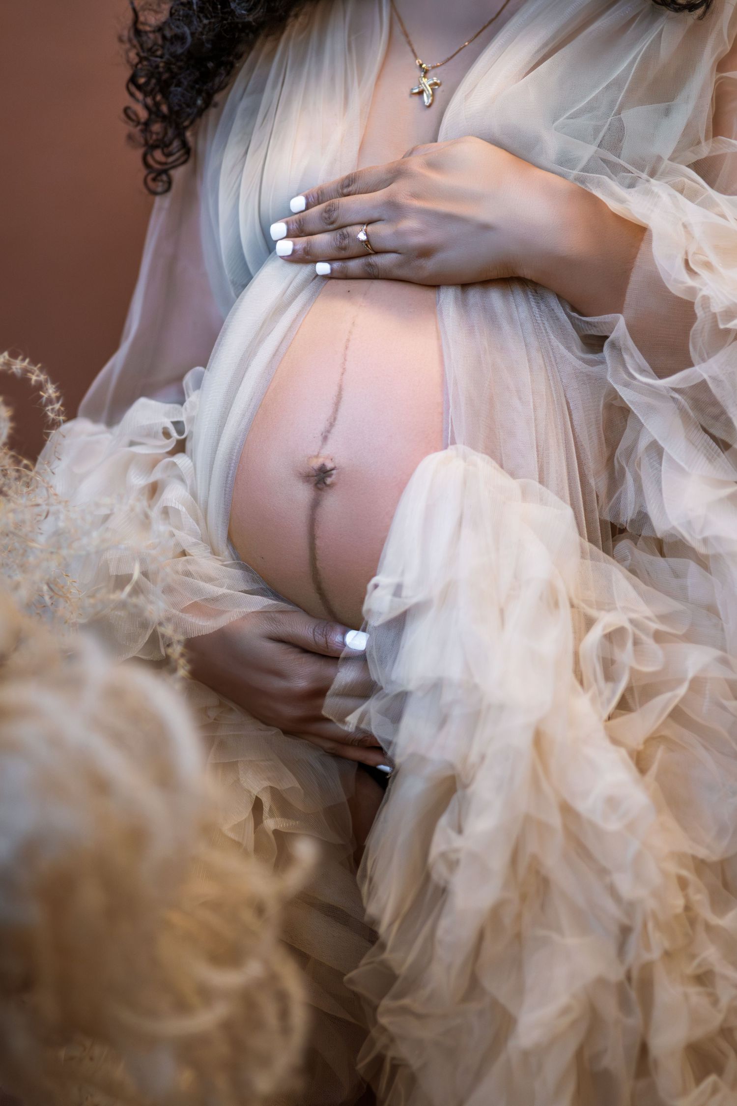 Artistic maternity photo series showing delicate tulle fabric draped over a pregnant belly with white manicured nails.