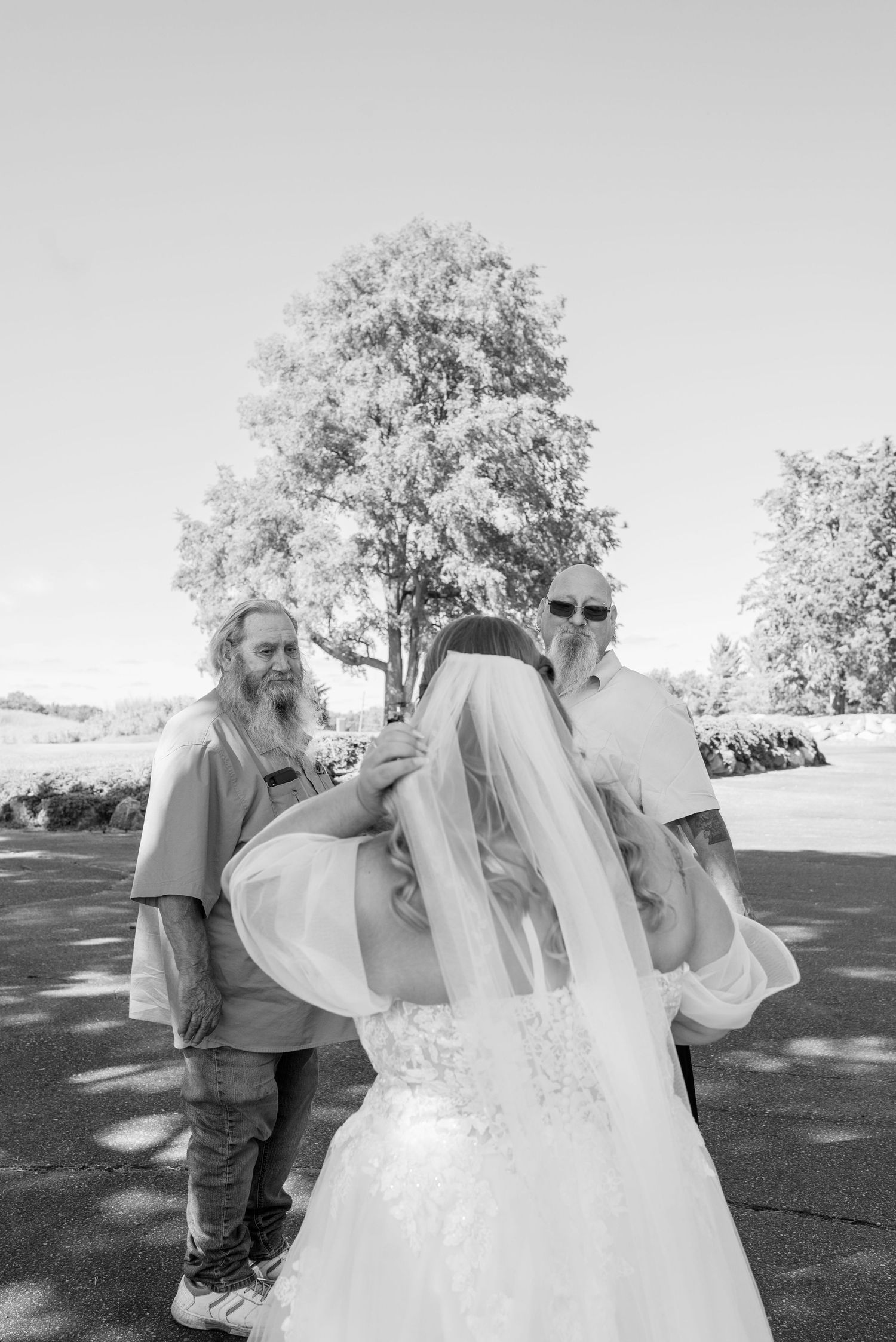 Black and white photo sequence showing two wedding guests enjoying their drinks together on a sunny day outdoors.