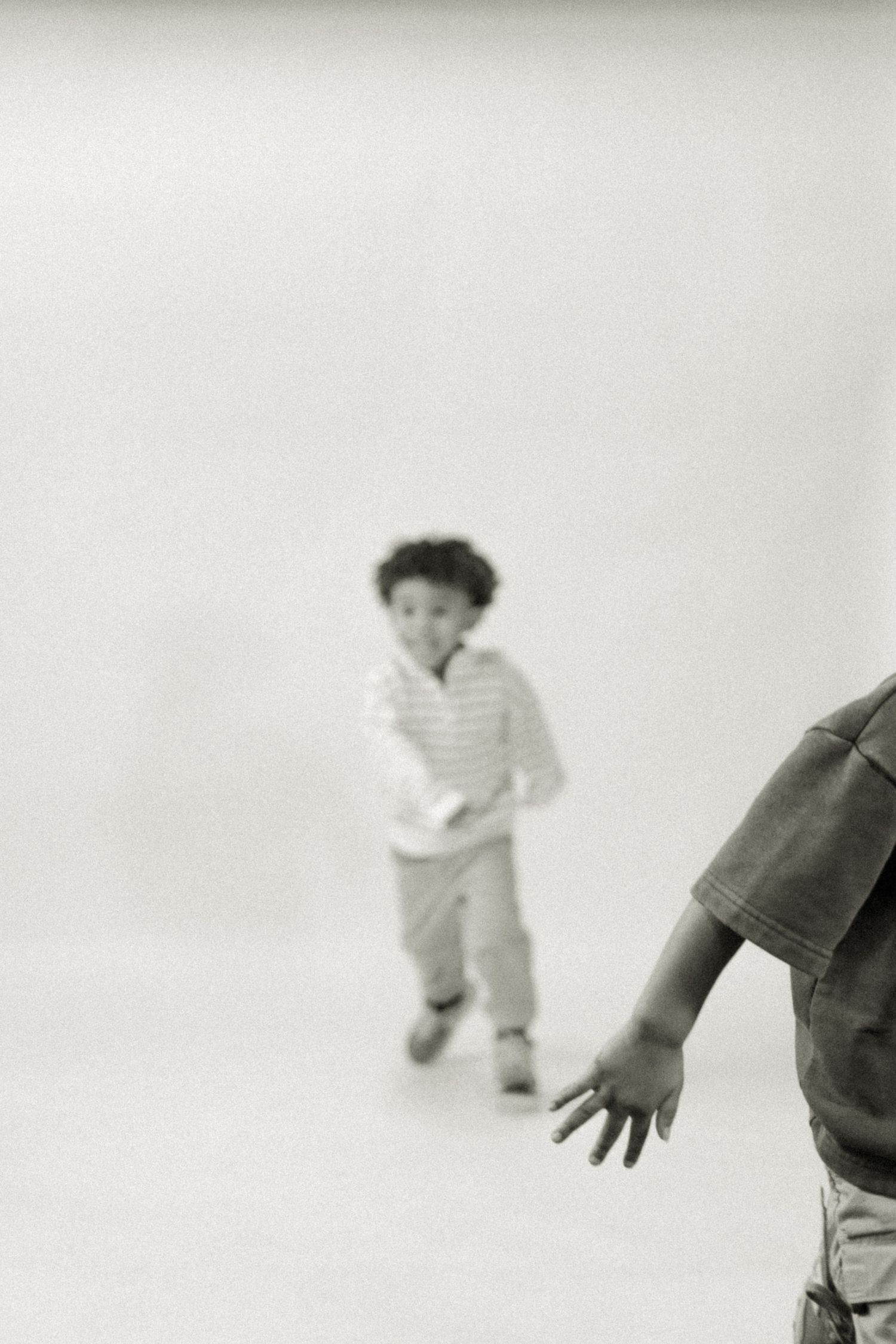 Two young boys playing and running in a bright white studio, captured in black and white photography.
