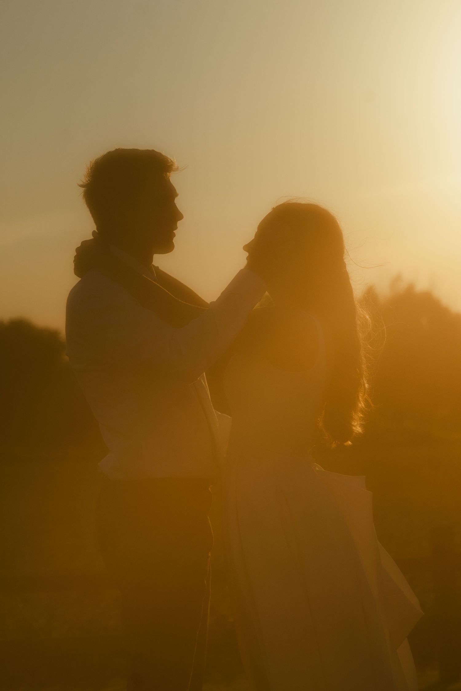 Romantic silhouette of a couple embracing at golden sunset, man gently touching woman's face outdoors.