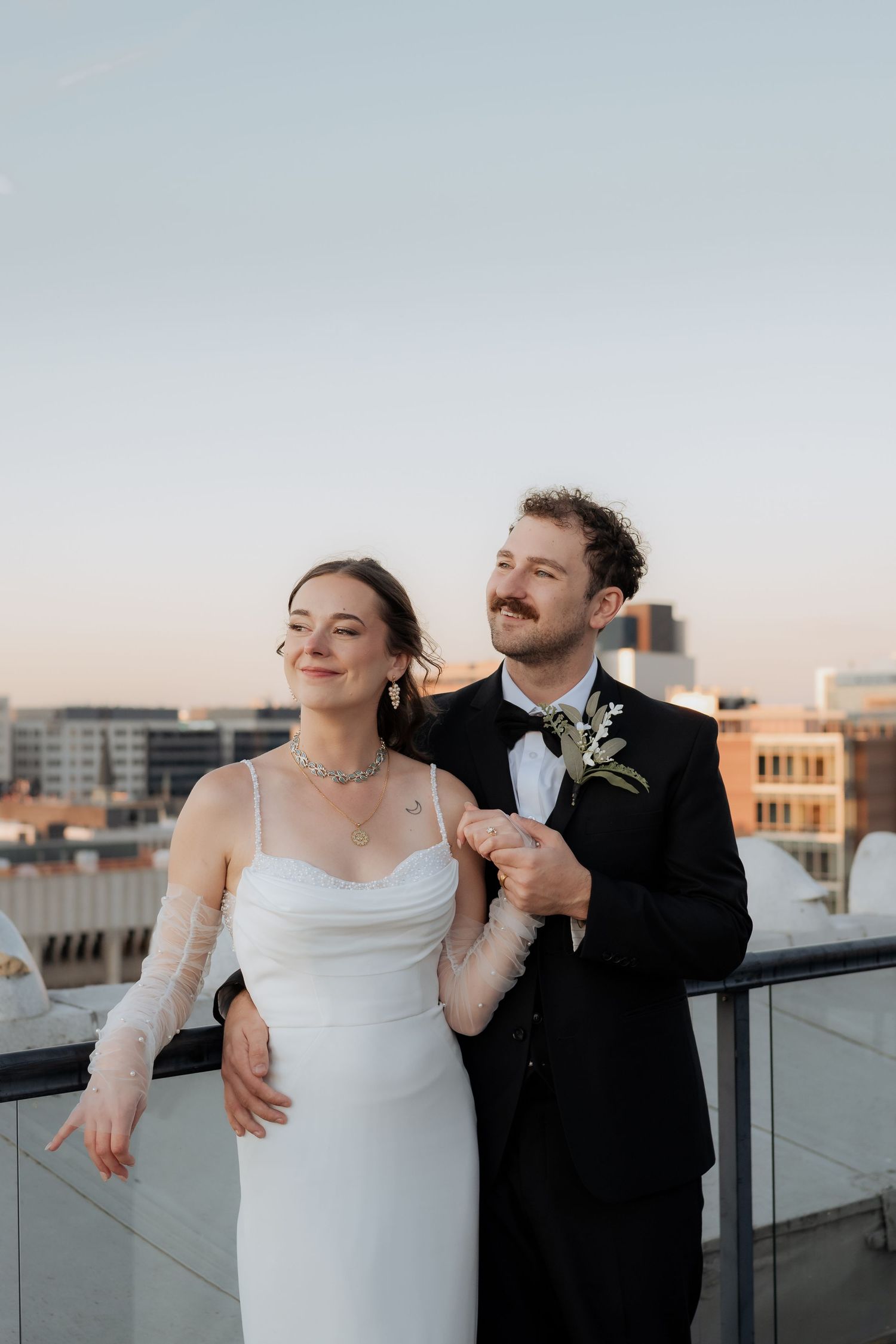 A couple shares romantic candid moments on a rooftop during sunset in their formal wedding attire.