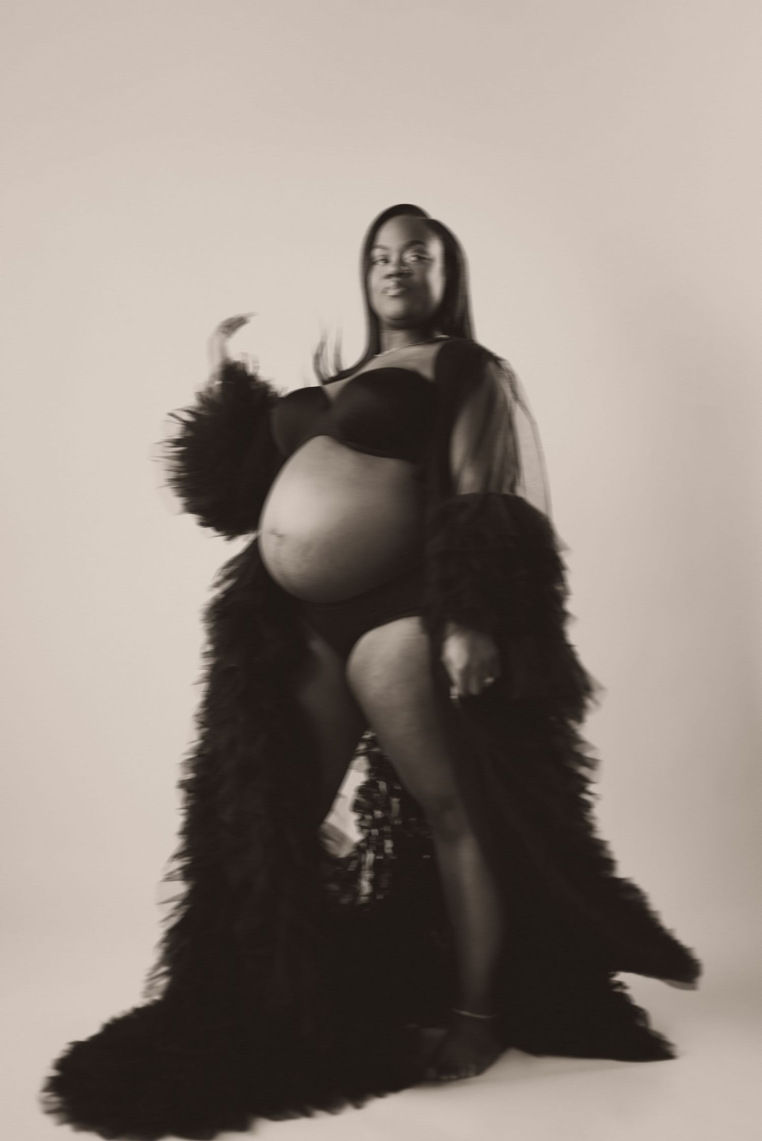 Elegant black and white maternity photo of a pregnant woman in a black robe and lingerie posing gracefully in studio.
