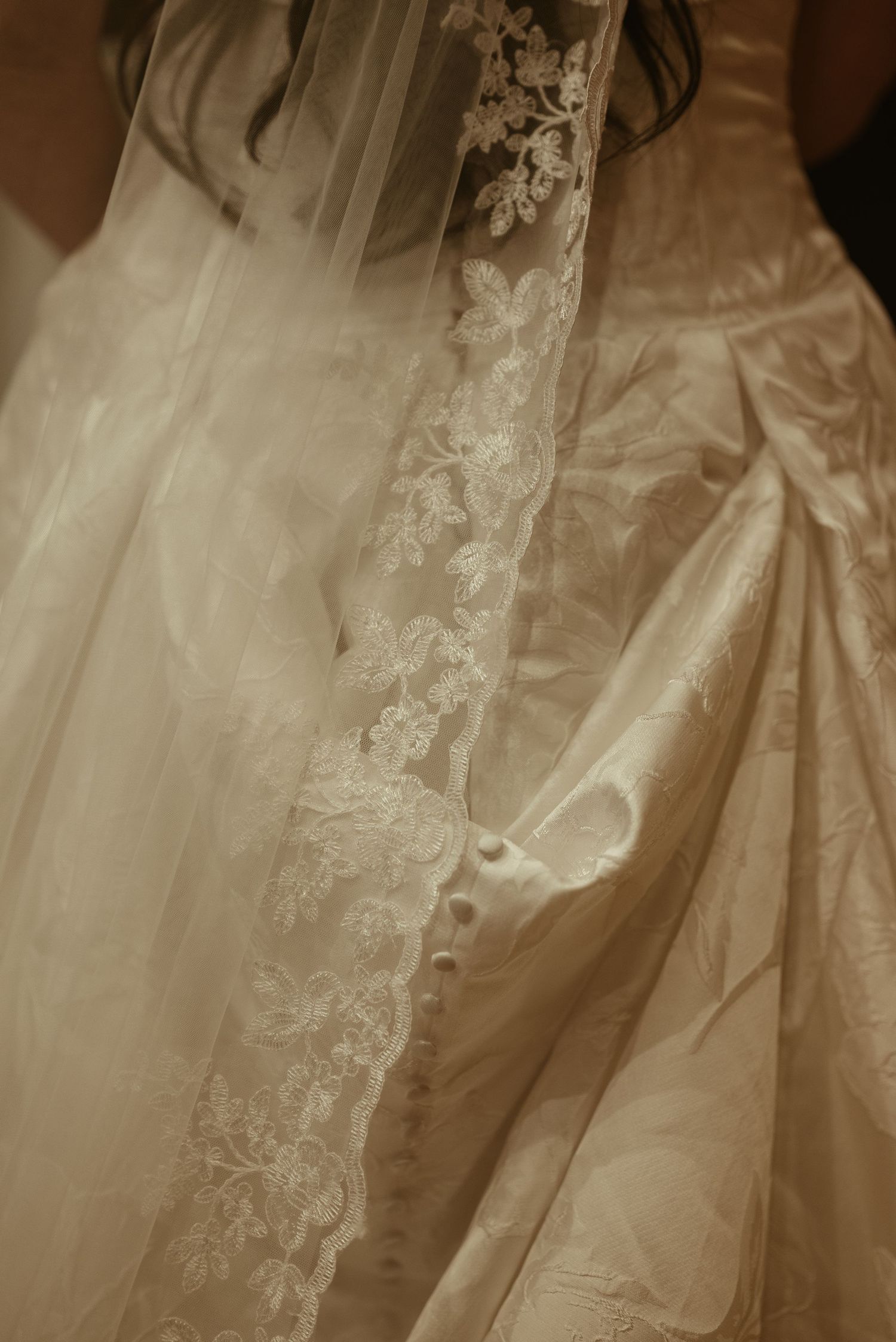 Close-up of an ivory wedding dress with delicate lace veil overlay featuring floral embroidery details.