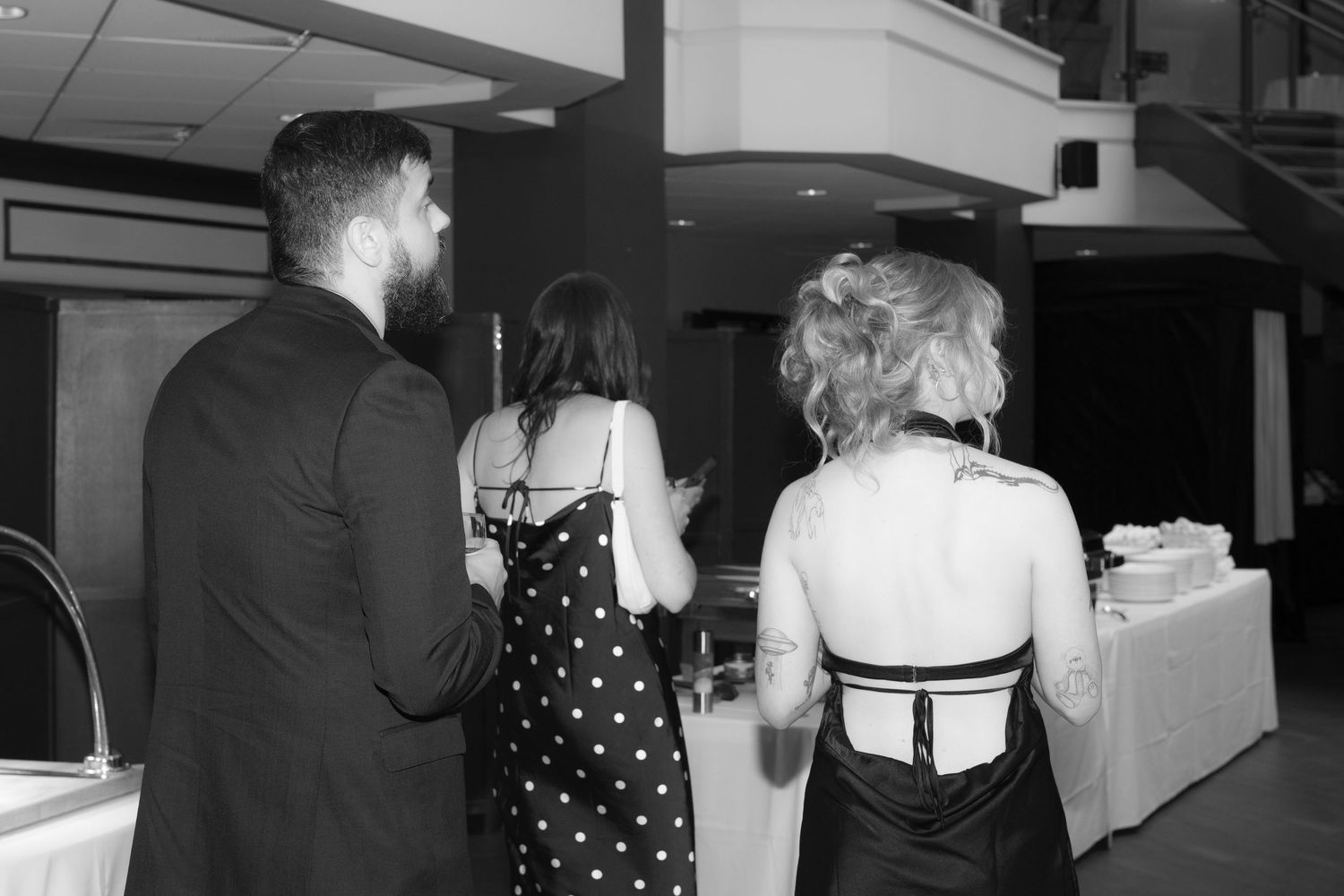 A vintage black and white photograph showing people in formal attire at an indoor social gathering.