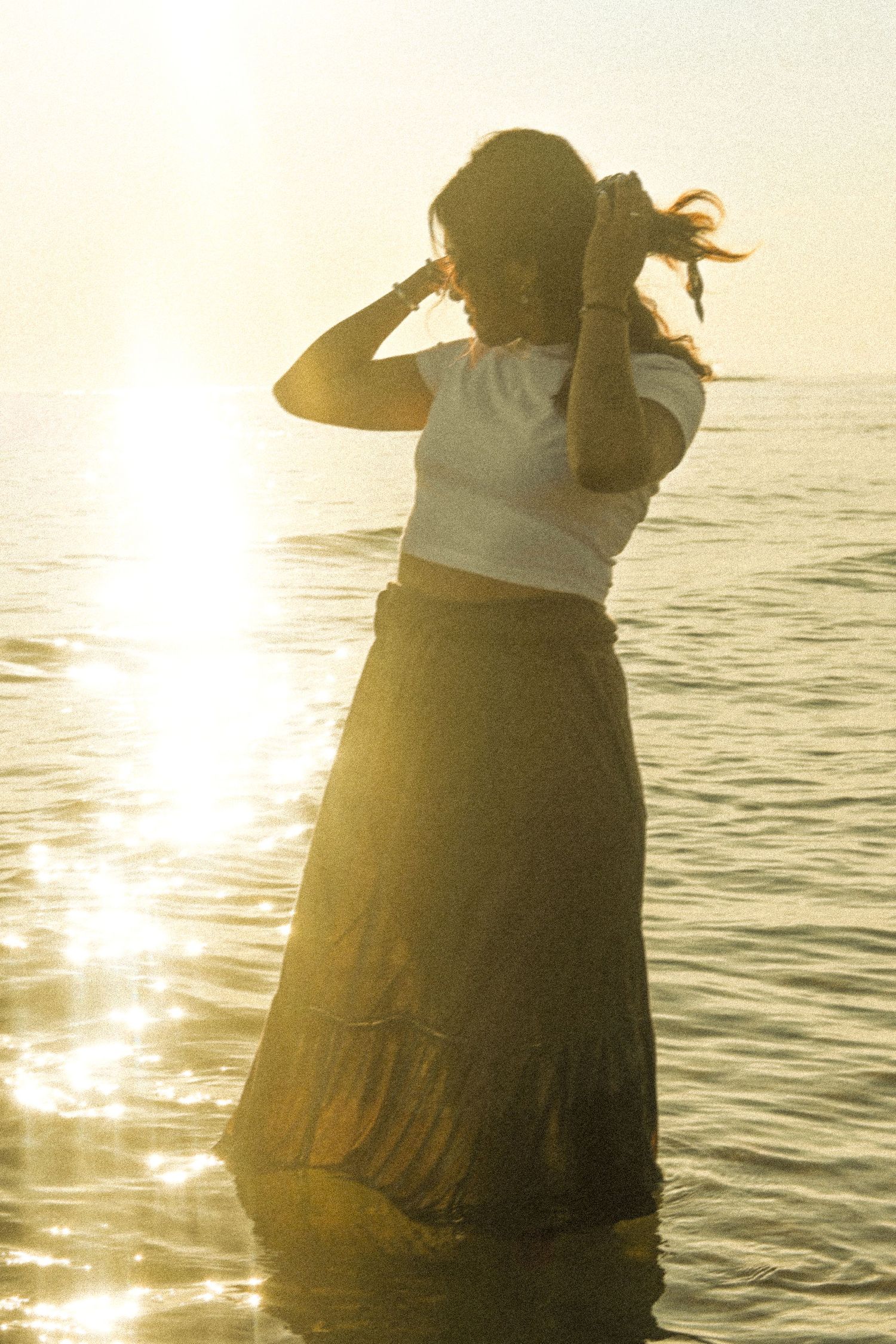 Silhouette against sunset over ocean wearing flowing skirt and creating artistic poses.