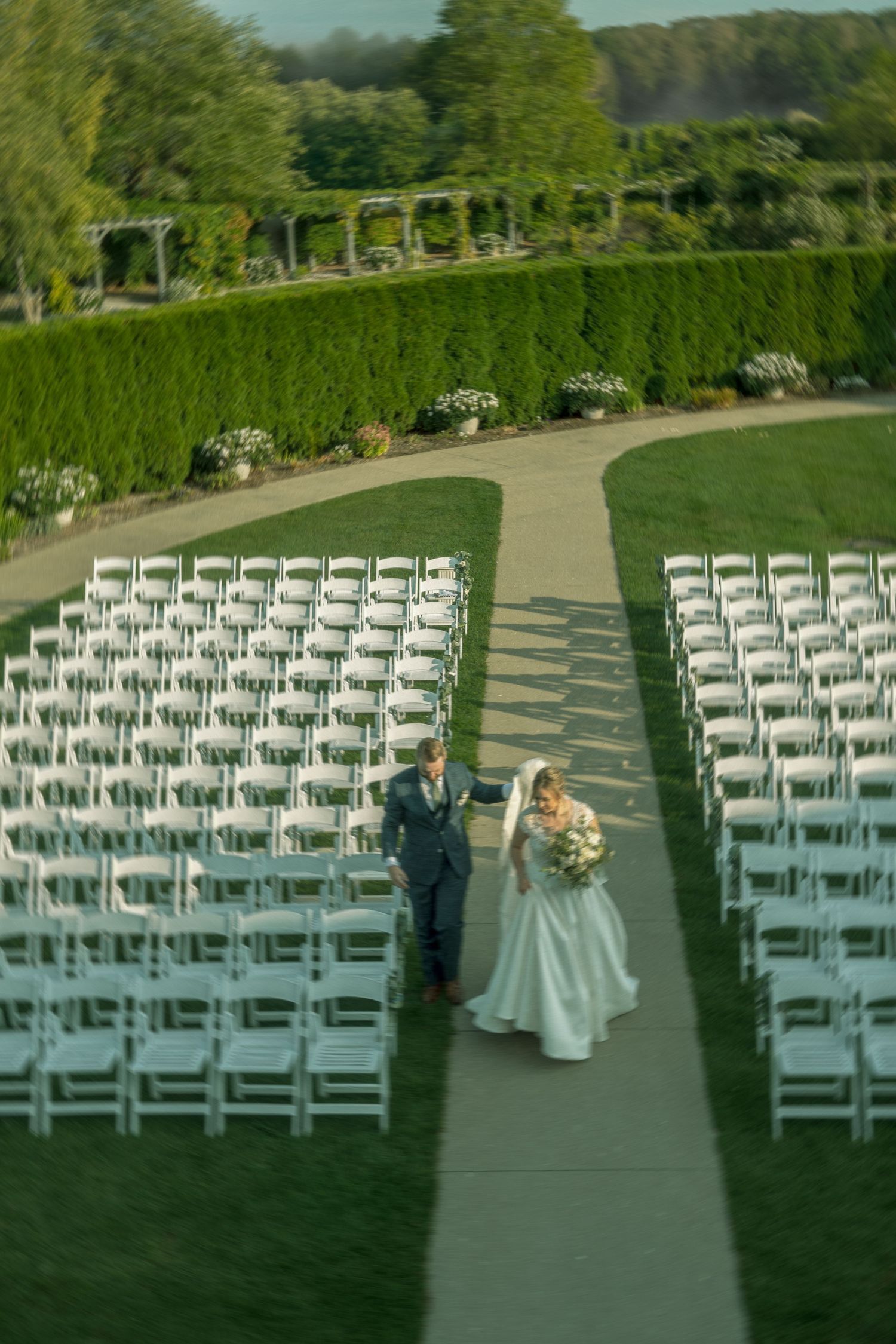A wedding ceremony setup outdoors with rows of white chairs arranged on a grassy lawn.