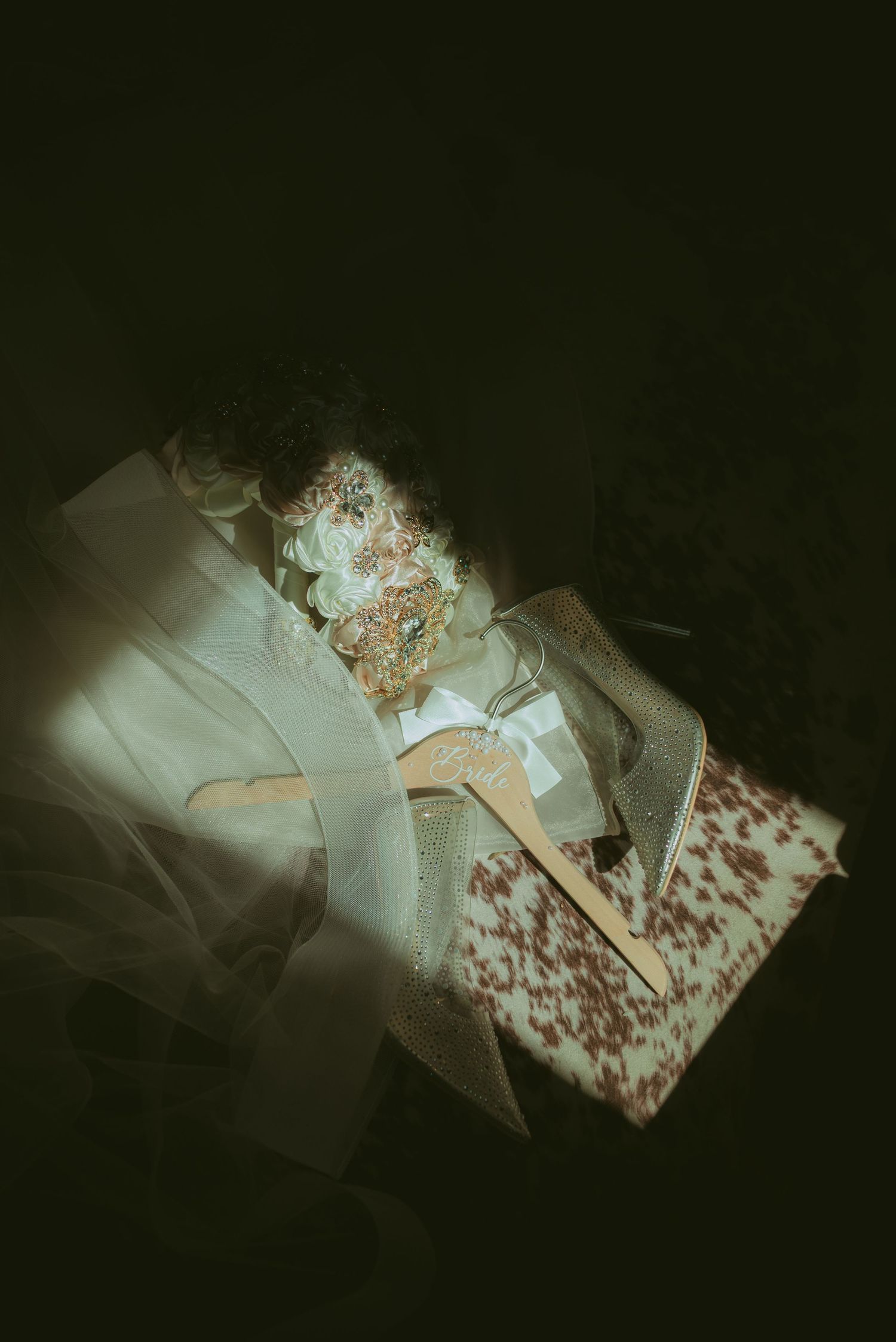 Elegant wedding accessories including glittery heels, floral details, and a veil arranged on a dark background.