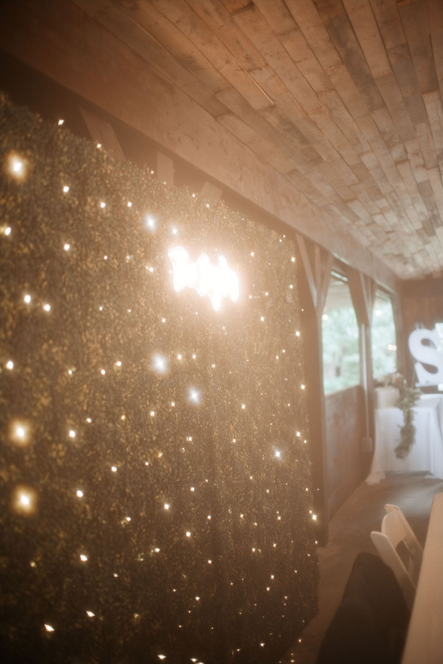 Sparkling fairy light curtain backdrop glowing warmly in an elegant event venue with wooden ceiling panels.