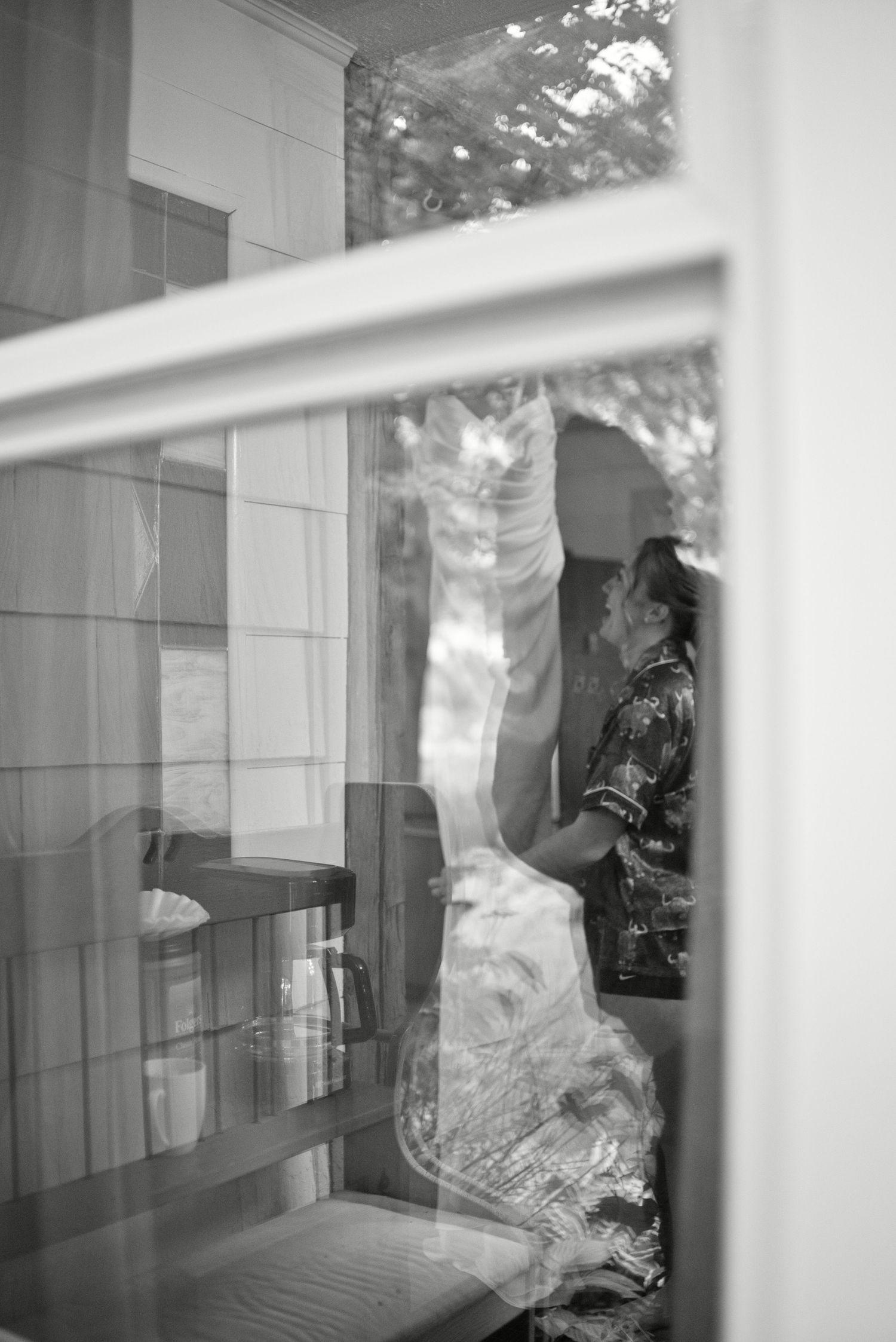 Black and white photo of a person reflected in a glass window, with trees visible in the background.